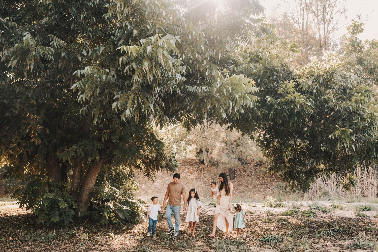 Stylish family enjoying a sunset photoshoot in a nature setting with golden light filtering through trees.
