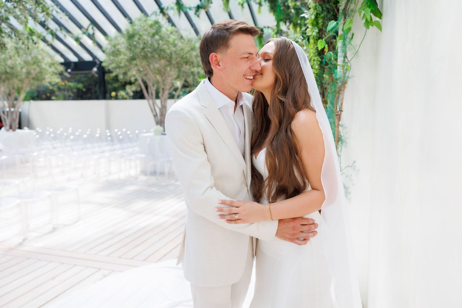 A couple in white attire embrace and kiss during their romantic outdoor wedding ceremony at Greenhouse Two Rivers in Missouri.