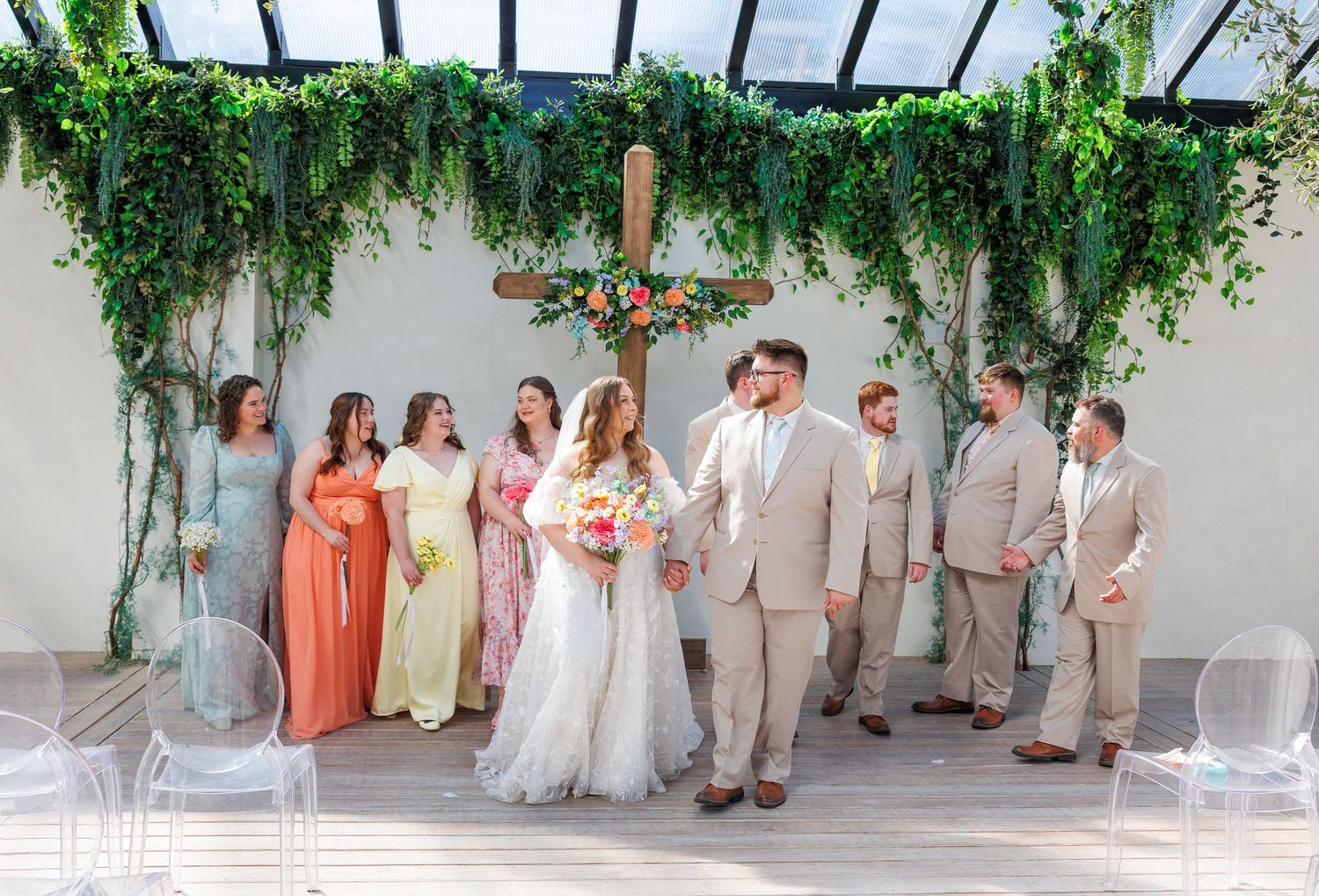 Wedding party members posed in coordinated peach and neutral tones against a lush greenhouse backdrop in Missouri by Janie Loftin.