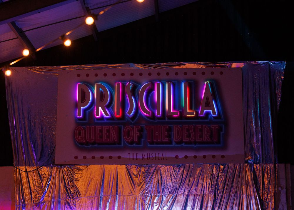 Colorful neon signs and stage lighting illuminate a theater or nightclub entrance with purple and pink hues.
