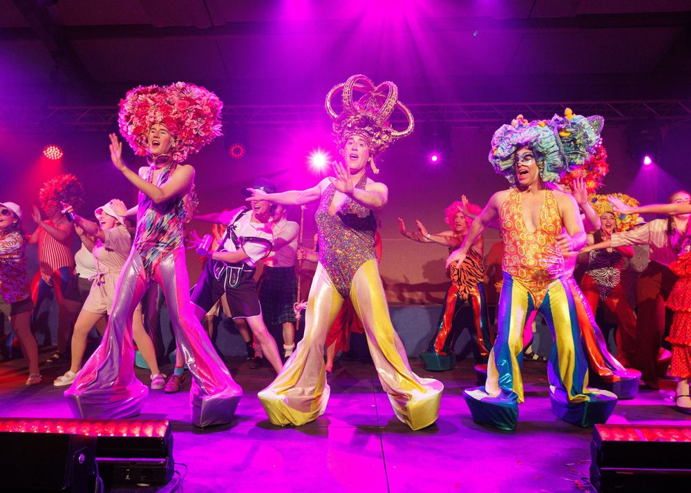 Dance ensemble performs a synchronized routine under vibrant pink and purple stage lights.