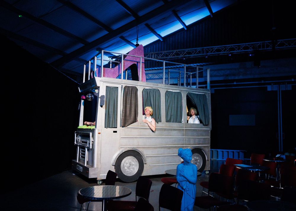 A dark industrial warehouse interior with blue lighting illuminating a large white vehicle or bus structure.