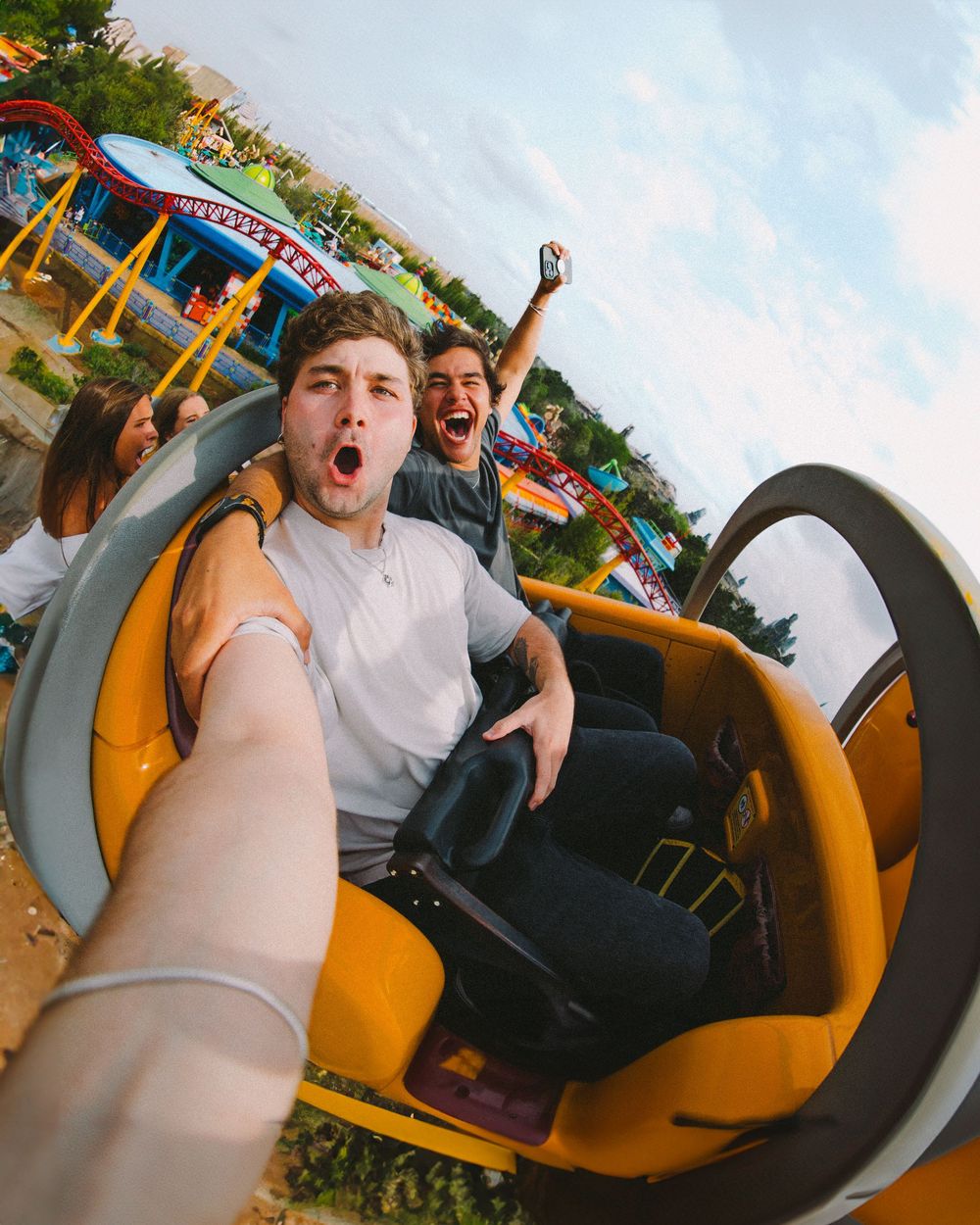 Two excited riders capture a thrilling selfie moment on a roller coaster at an amusement park.