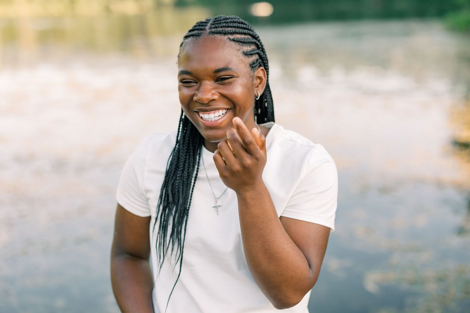Someone with long braided hair laughs joyfully while wearing a white t-shirt outdoors in natural lighting.