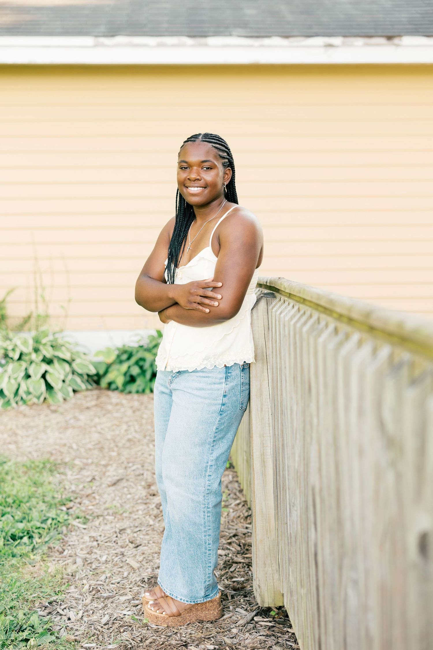 Candid outdoor portrait against wooden fence in natural light wearing white tank top and denim jeans.