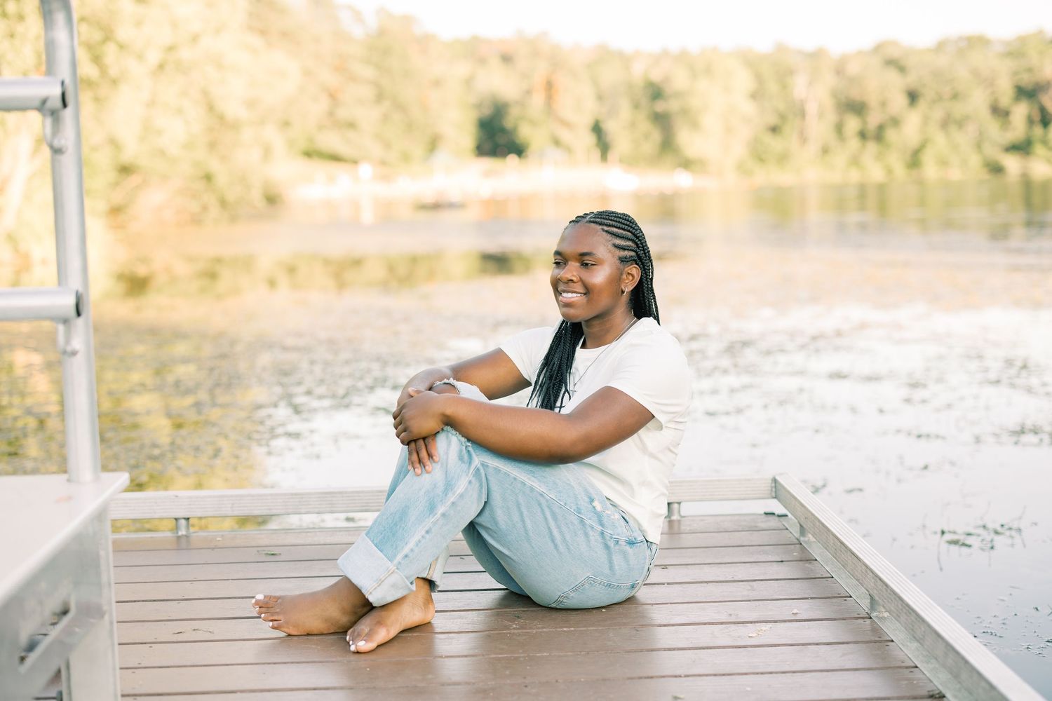 Someone sits peacefully on a wooden dock overlooking a serene lake on a sunny afternoon.
