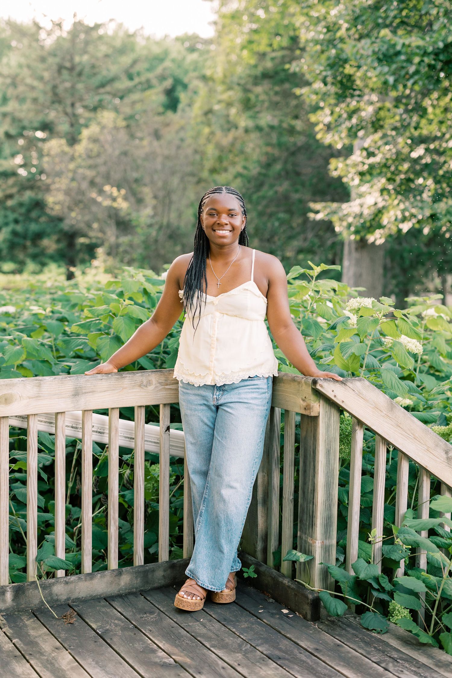 A casual outdoor photoshoot on a wooden deck surrounded by lush greenery and trees.