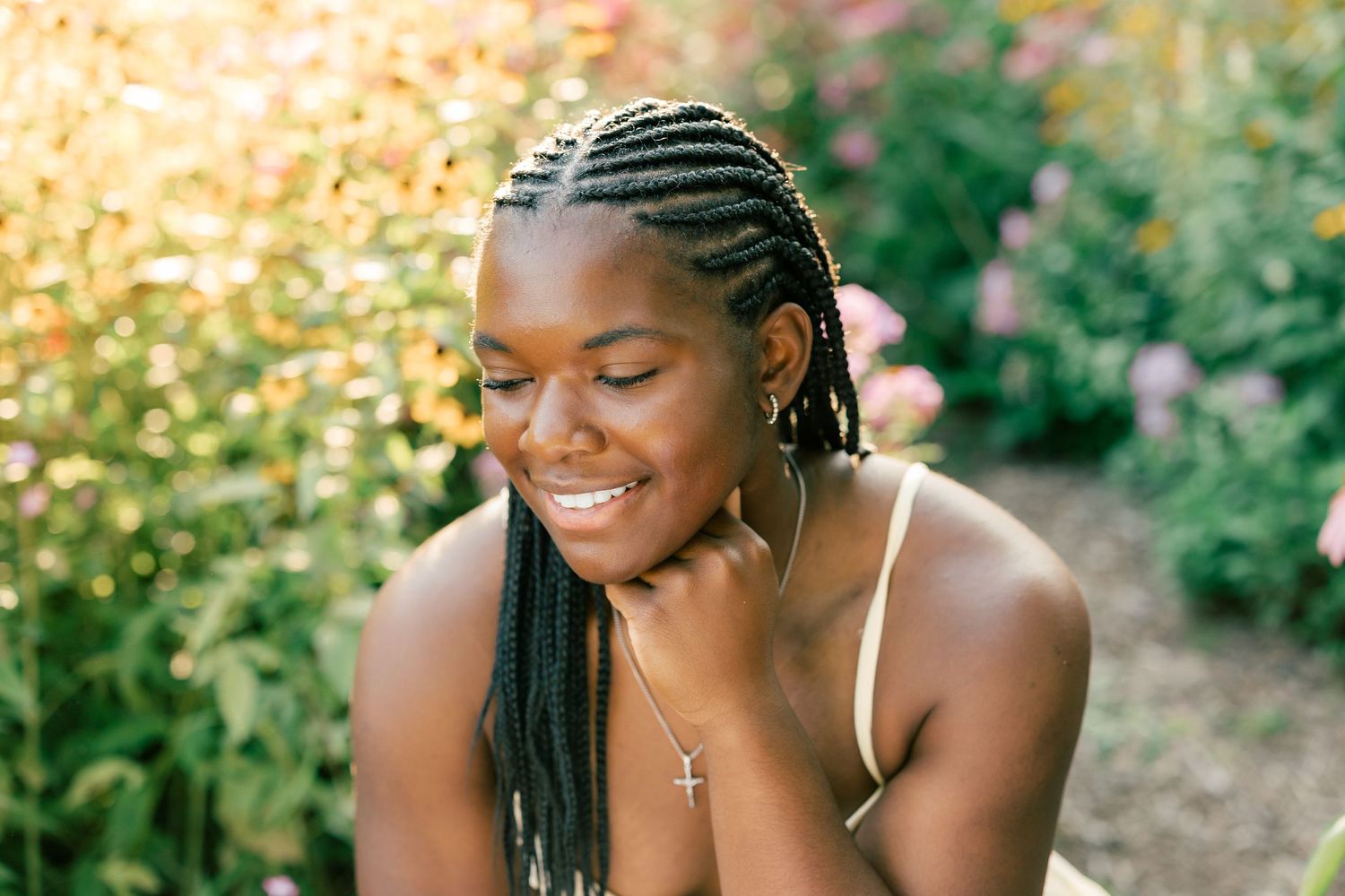 Woman with braided hair laughs joyfully while posing outdoors in natural sunlit setting.