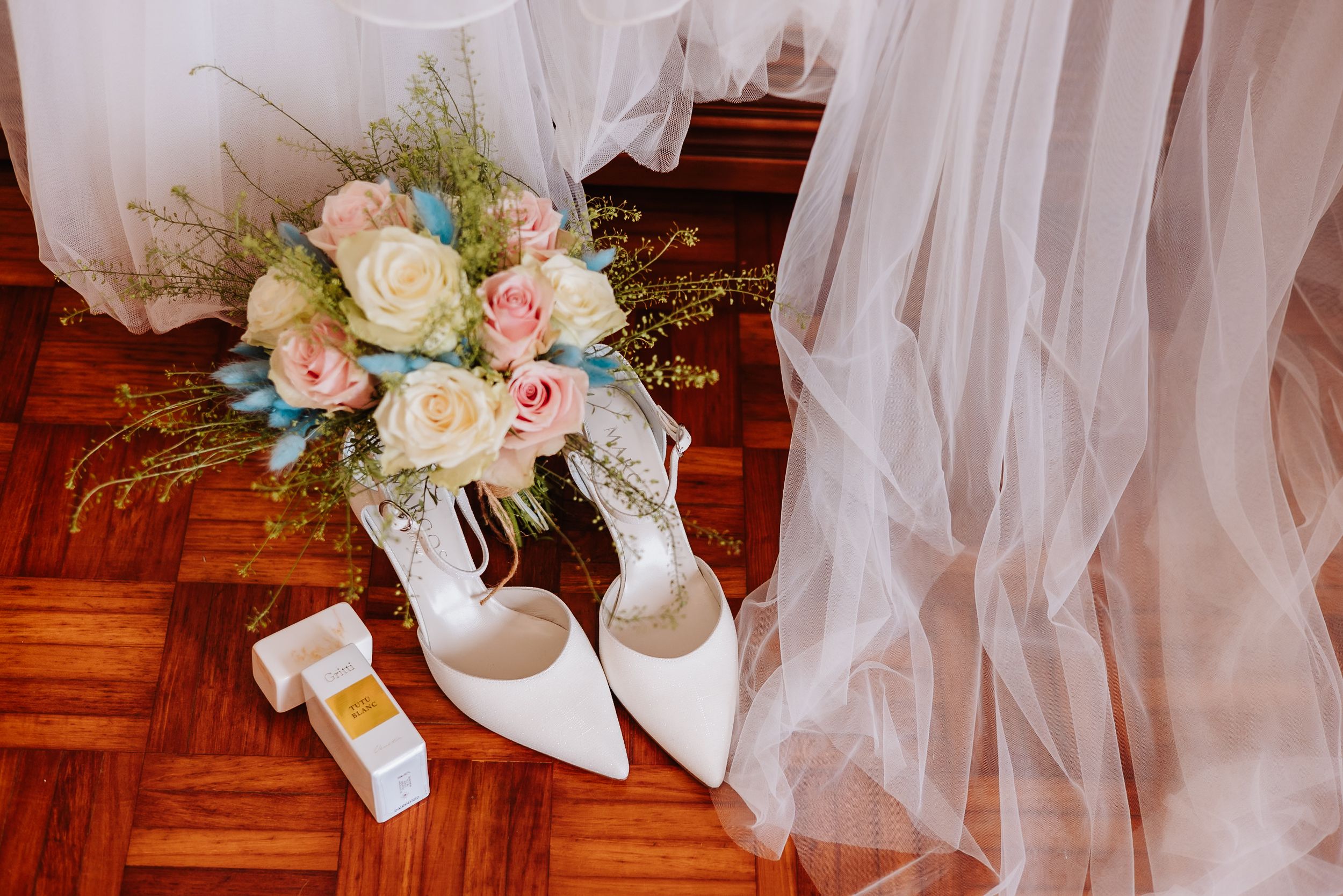 White tulle bridal veil and delicate pink rose bouquet arranged on wooden flooring.