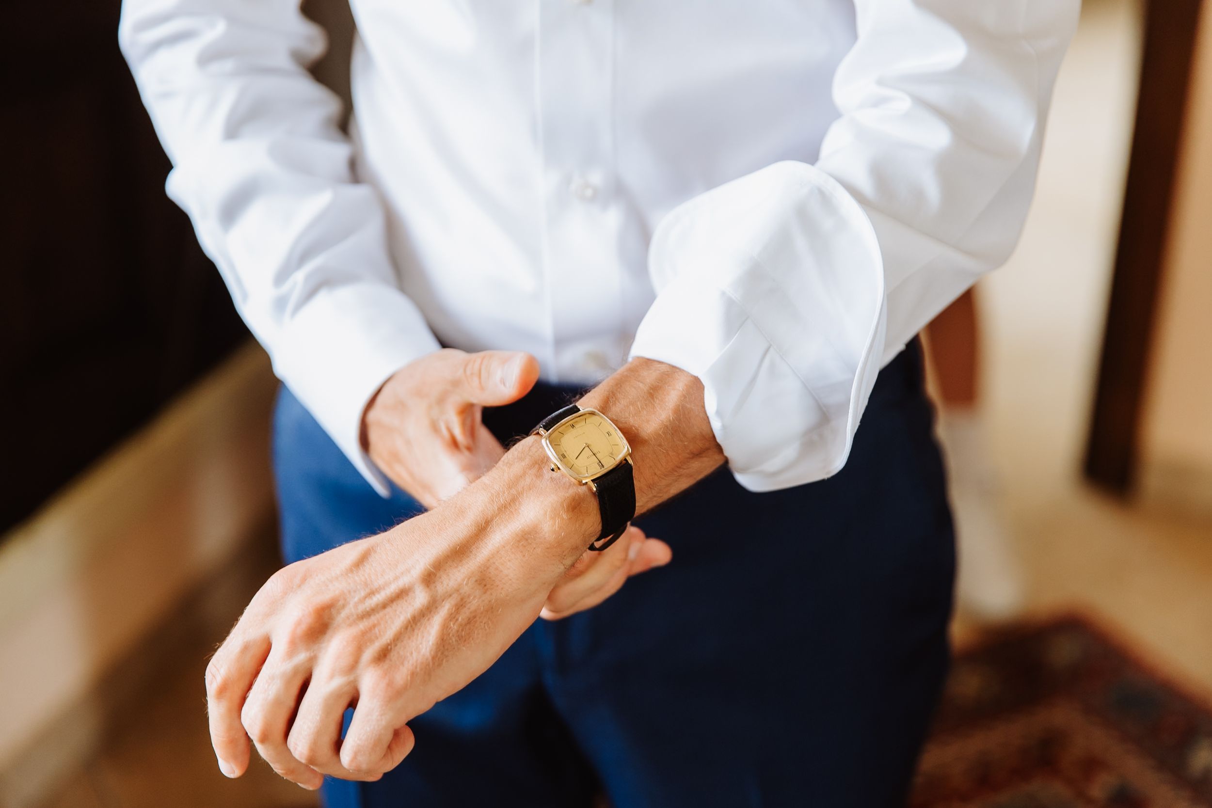 Hands adjusting formal white shirt cuffs and sleeves on a wooden background.