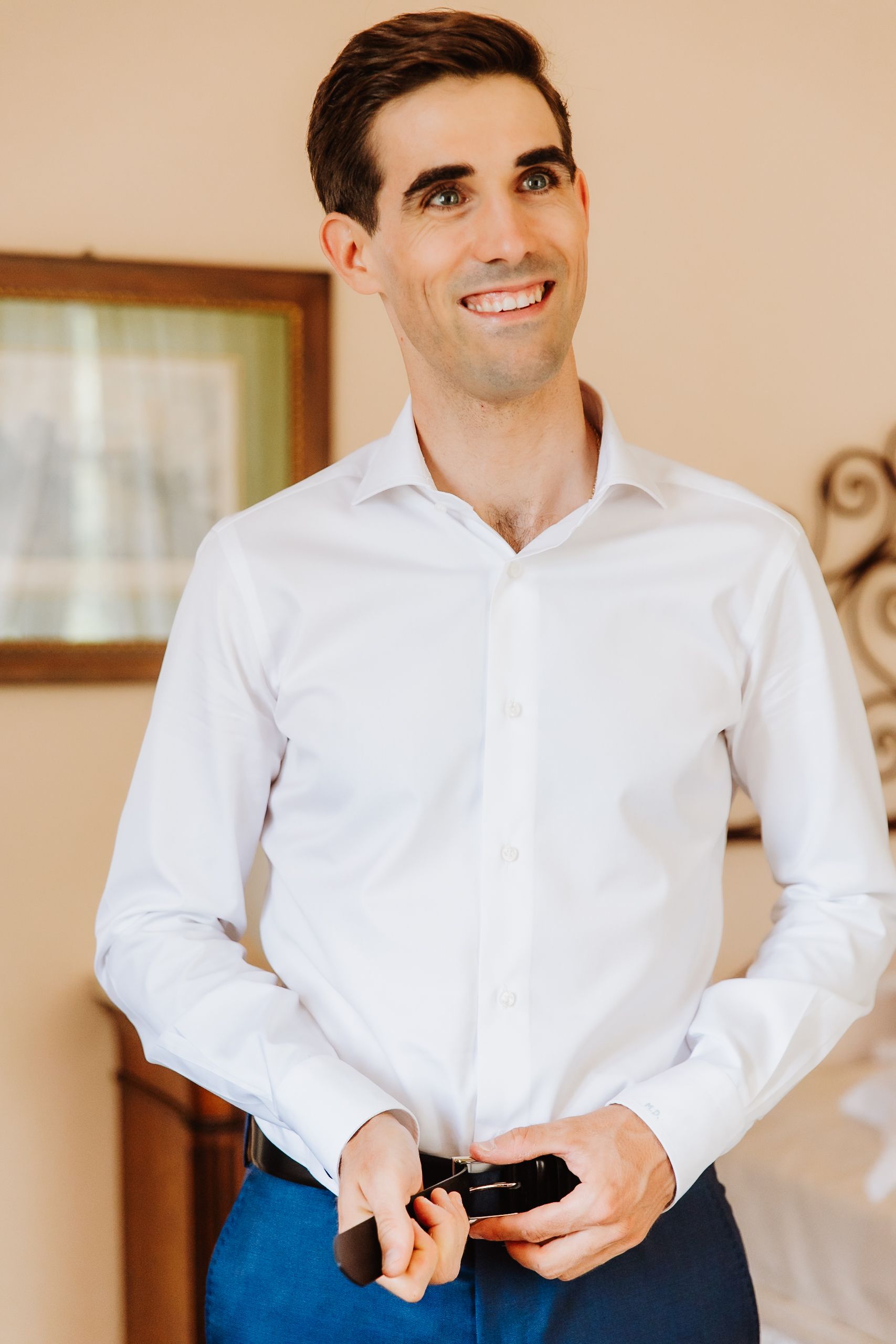 A person wearing a crisp white button-down shirt buttons up their cuffs while getting dressed.