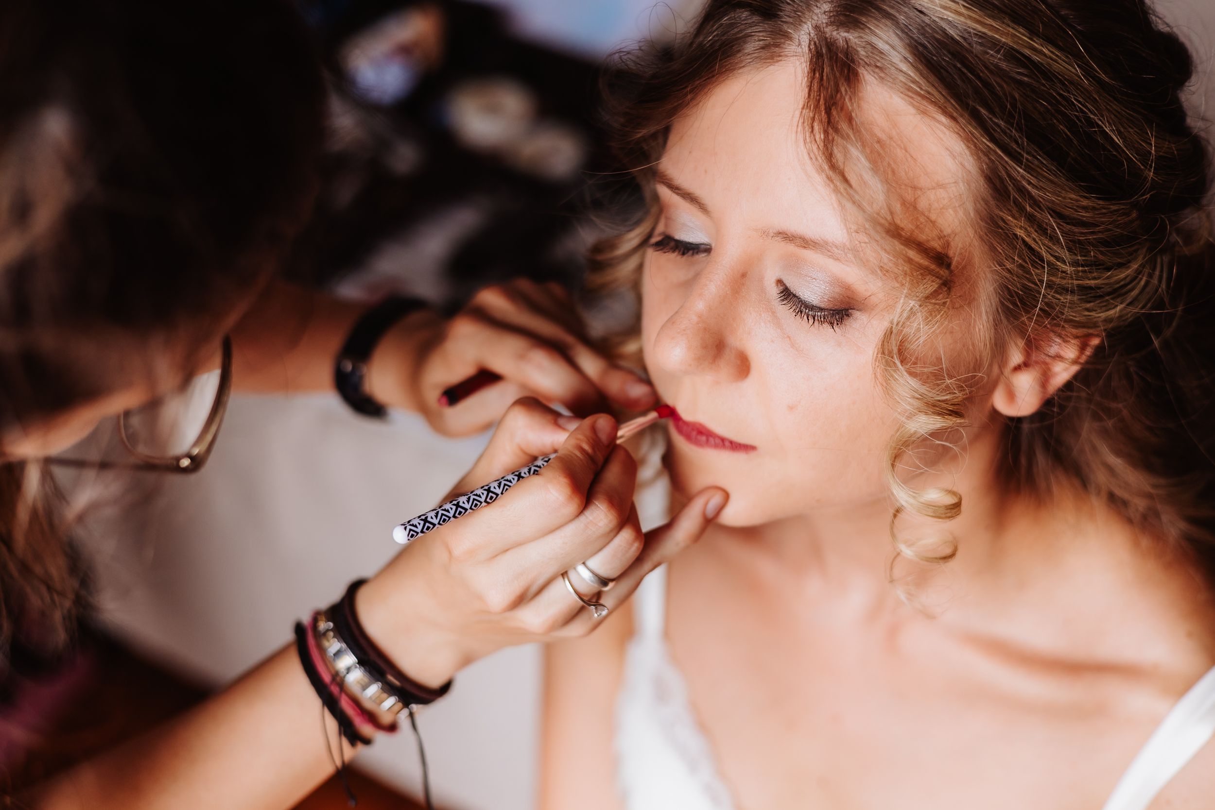Professional makeup artist carefully applies lipstick during bridal beauty preparation in warm lighting.
