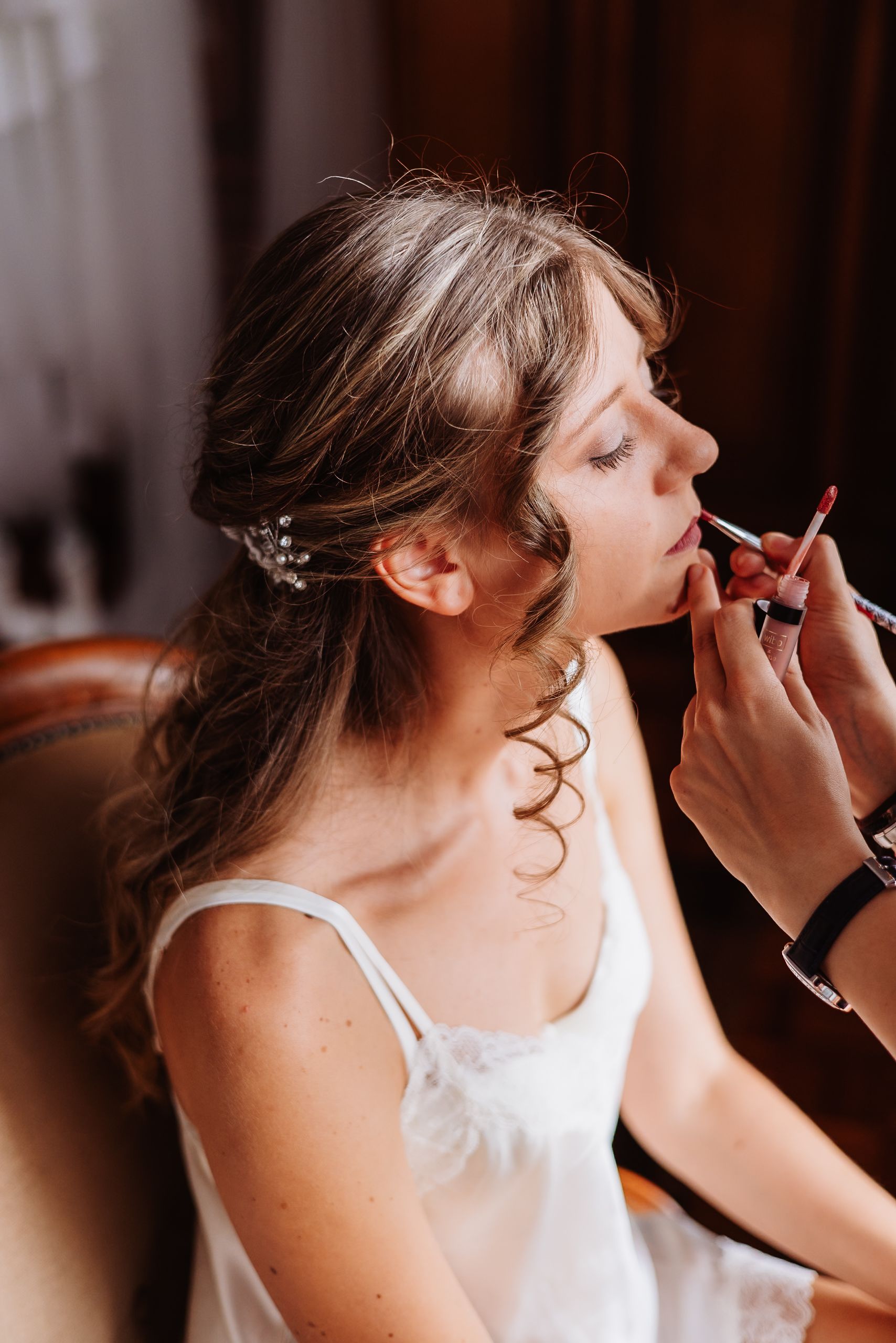 A makeup artist applies eye makeup to someone wearing a white tank top during a beauty preparation session.