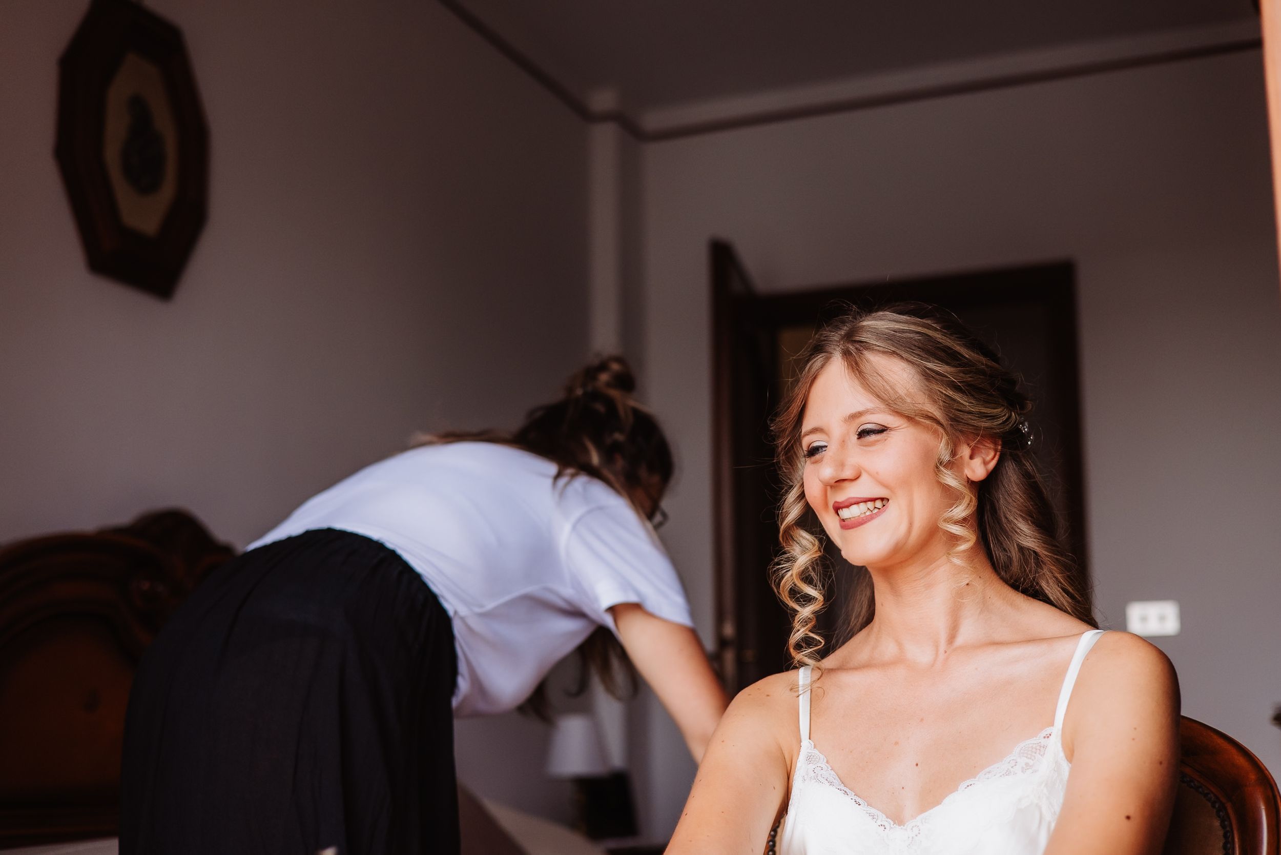 A joyful bride in a white wedding dress laughs while getting ready on her wedding day.