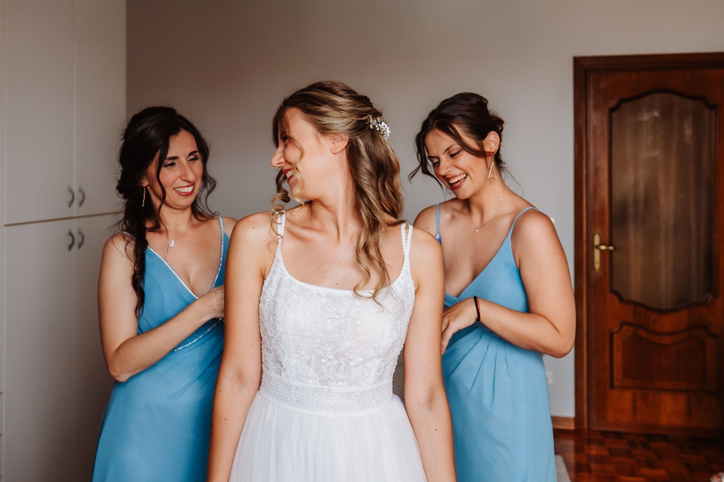 Three bridesmaids in turquoise dresses laugh and share a candid moment with the bride in her white gown.