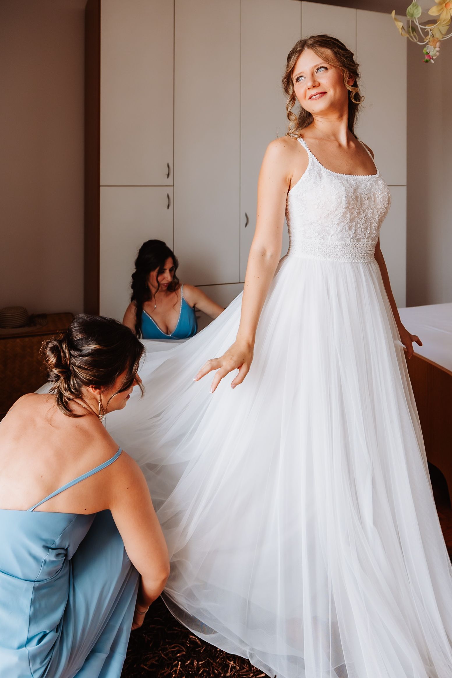 Bridesmaids in light blue dresses help adjust a flowing white wedding gown in a bridal preparation sequence.