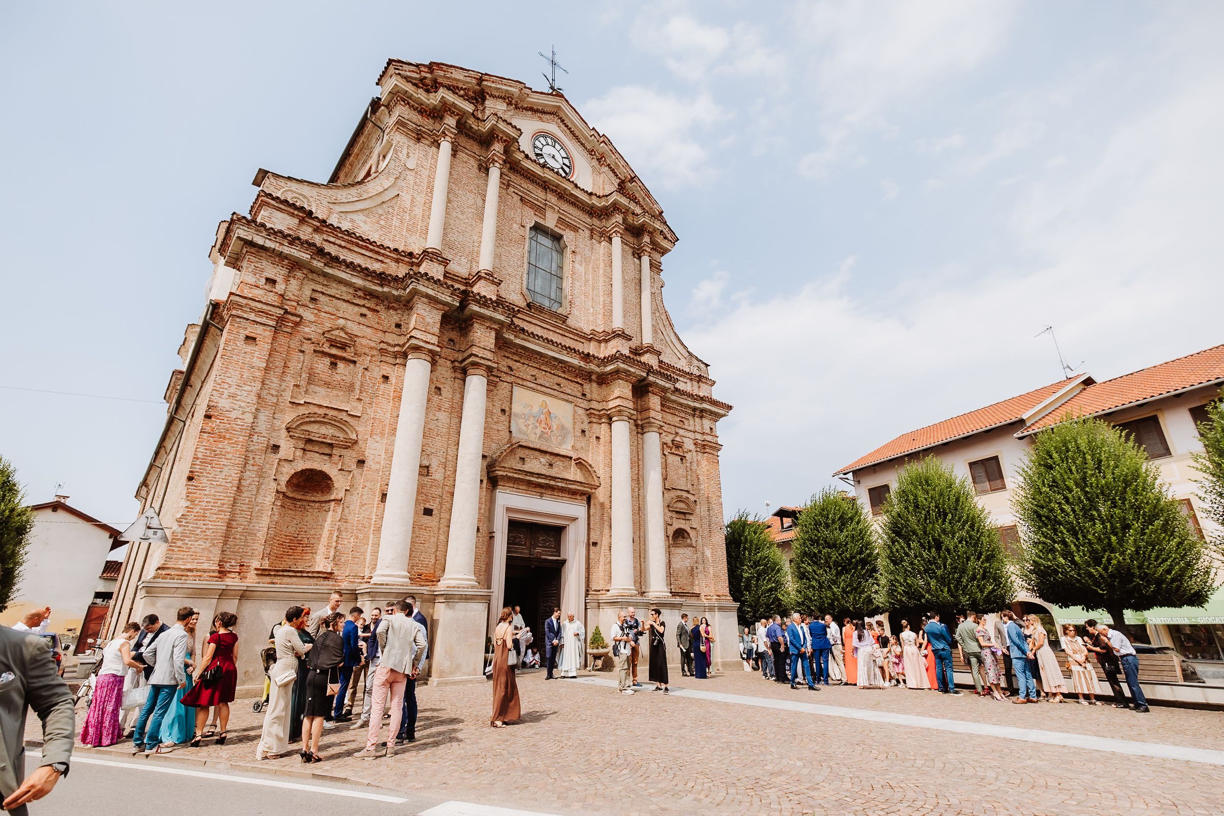 Elegant European church facade with ornate Baroque architecture and gathered crowd outside during a daytime event.