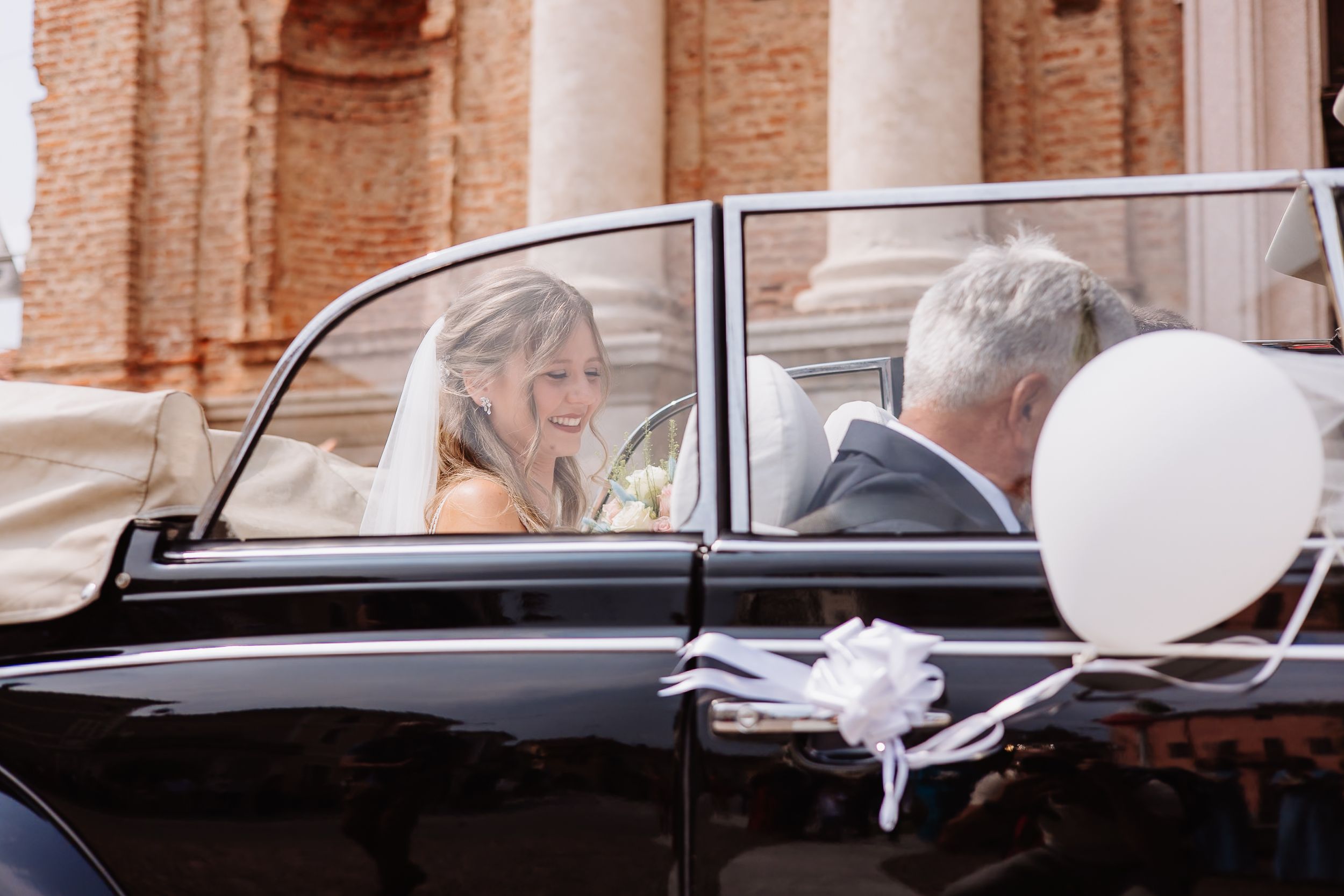 A row of classic black vintage cars decorated with white ribbons line up for a wedding ceremony.