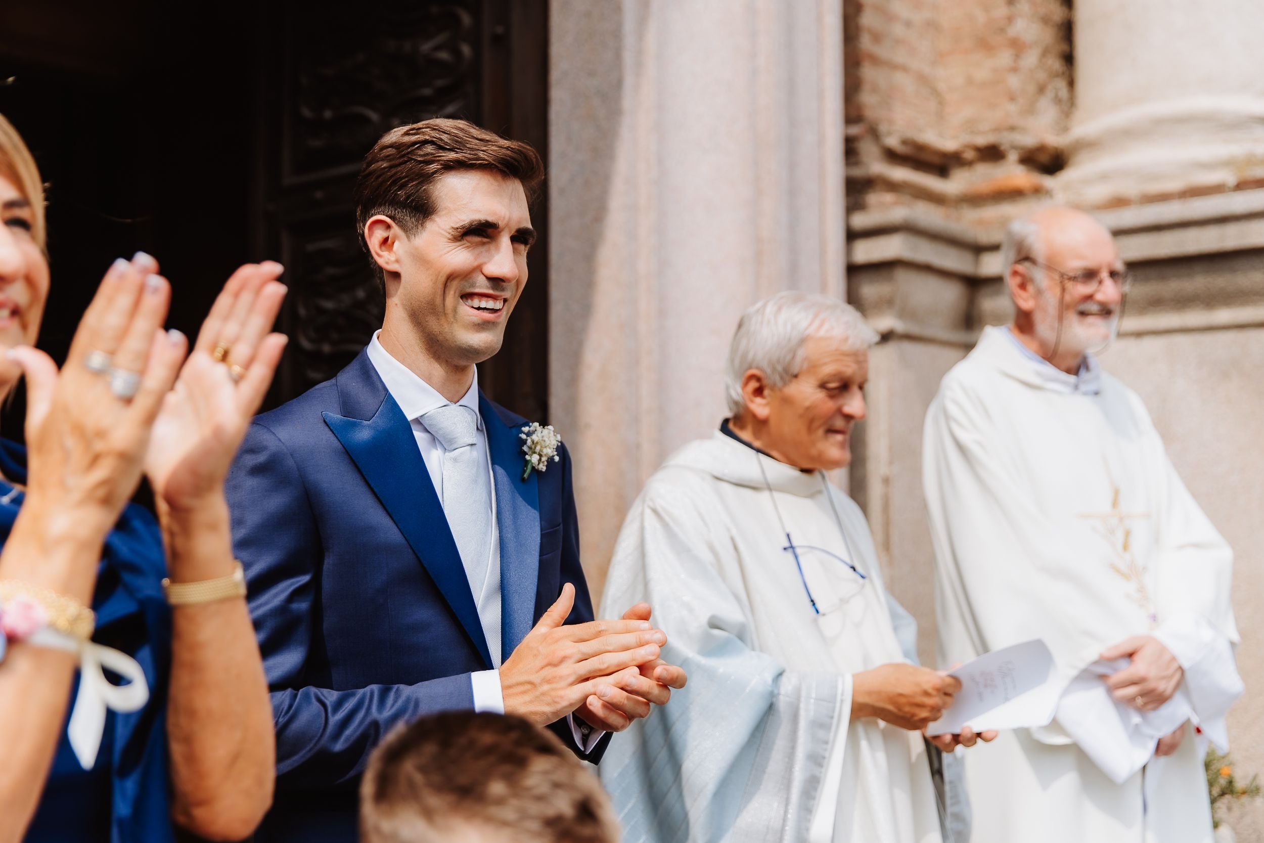 Group of people clapping and celebrating at a formal church ceremony with clergy members in white robes.