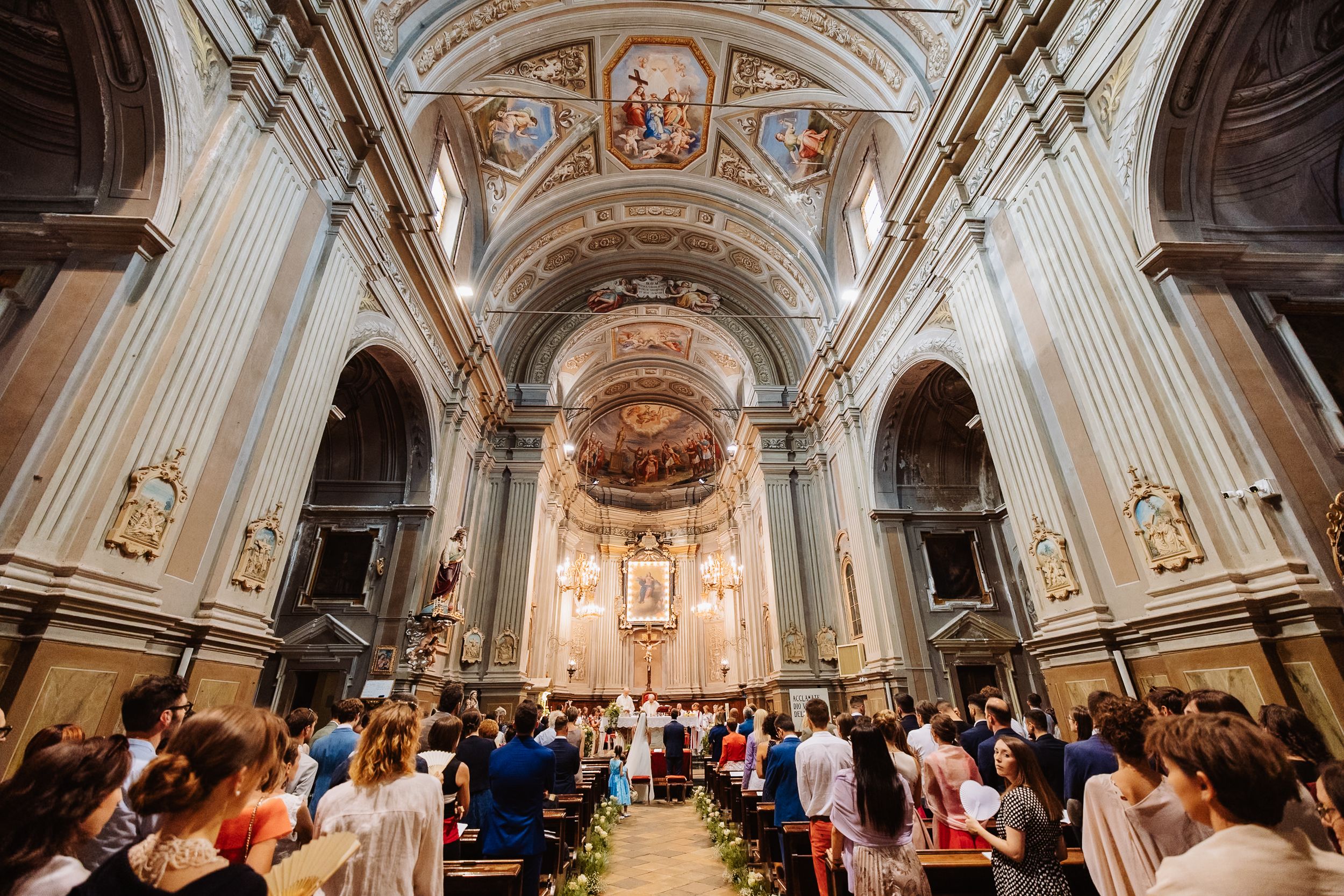 Interior panoramic view of an ornate Catholic church with classical baroque architecture and painted ceiling details.