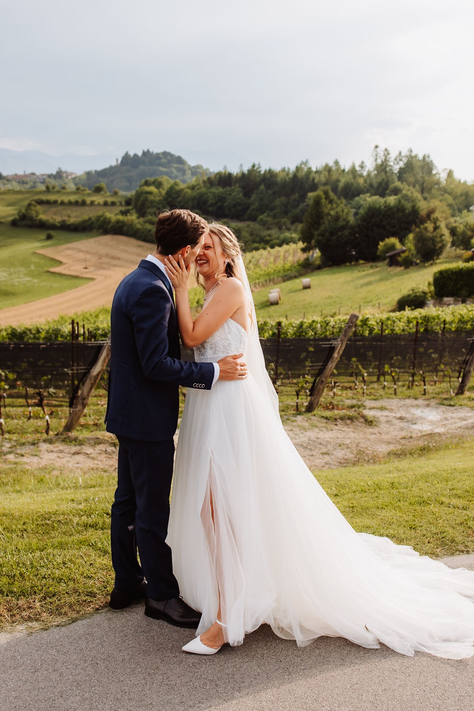 Romantic winery wedding portraits show newlyweds embracing outdoors with vineyard landscape and rolling hills in background.