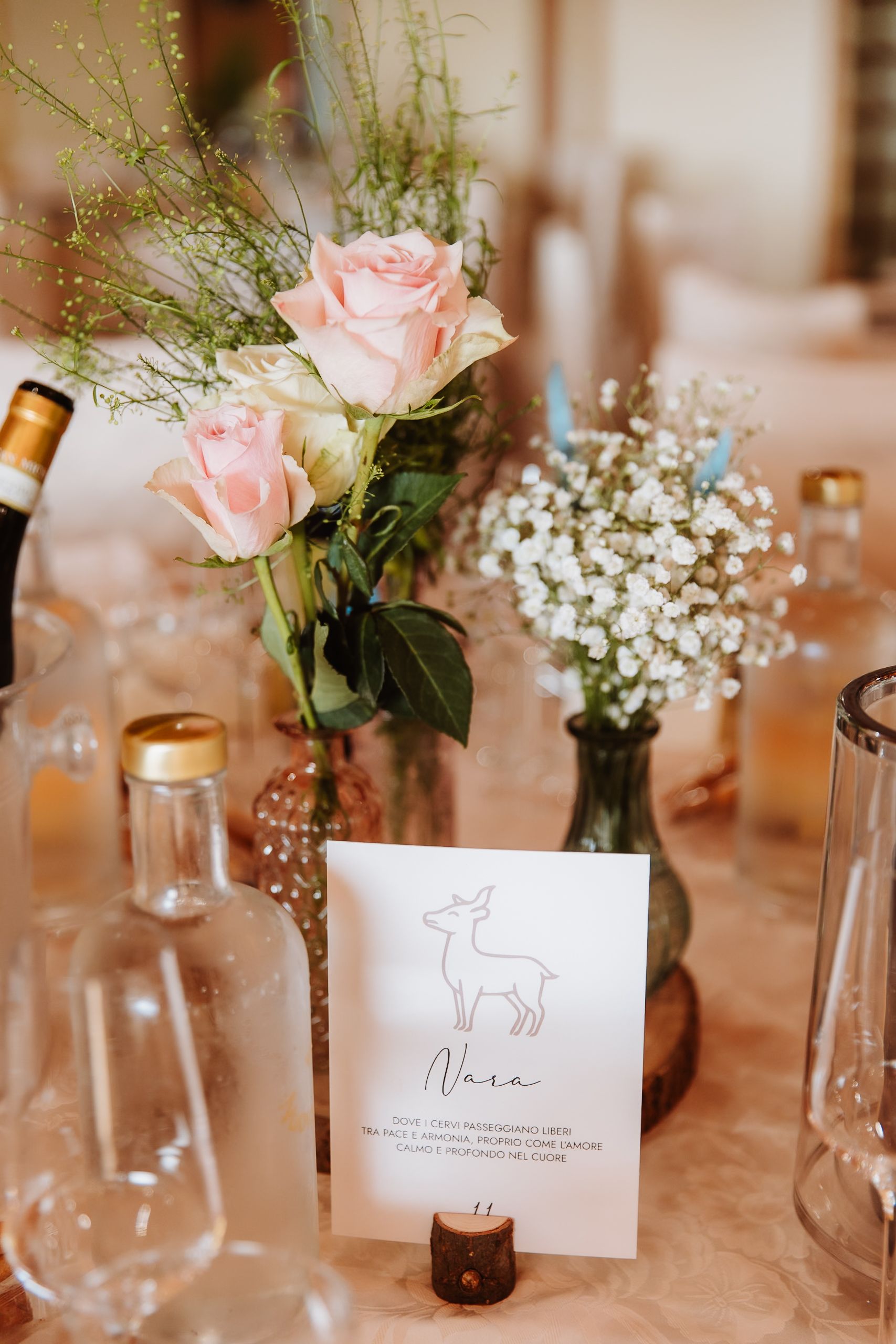 Elegant table setting with pink roses and baby's breath in glass vases alongside wine glasses and place cards.