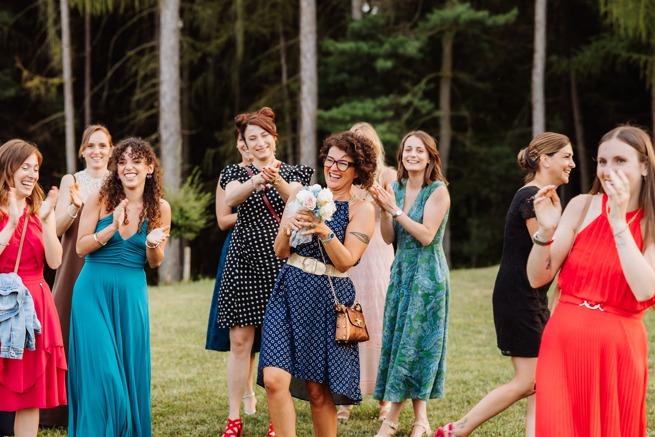 Group of friends in colorful dresses gather outdoors for a summer celebration in a park setting.