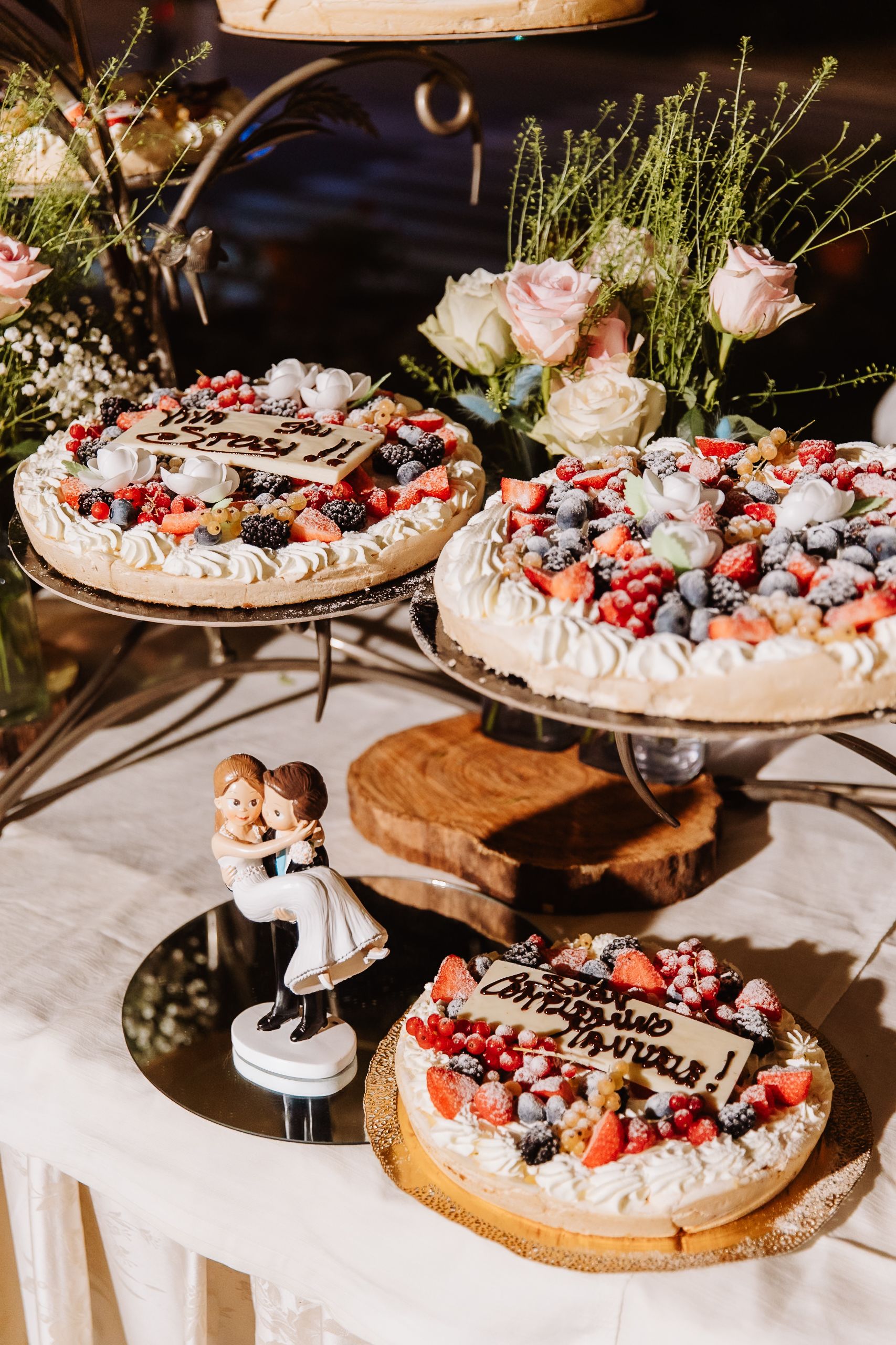 Wedding cake display decorated with fresh berries, roses and delicate garnishes arranged on wooden stands.