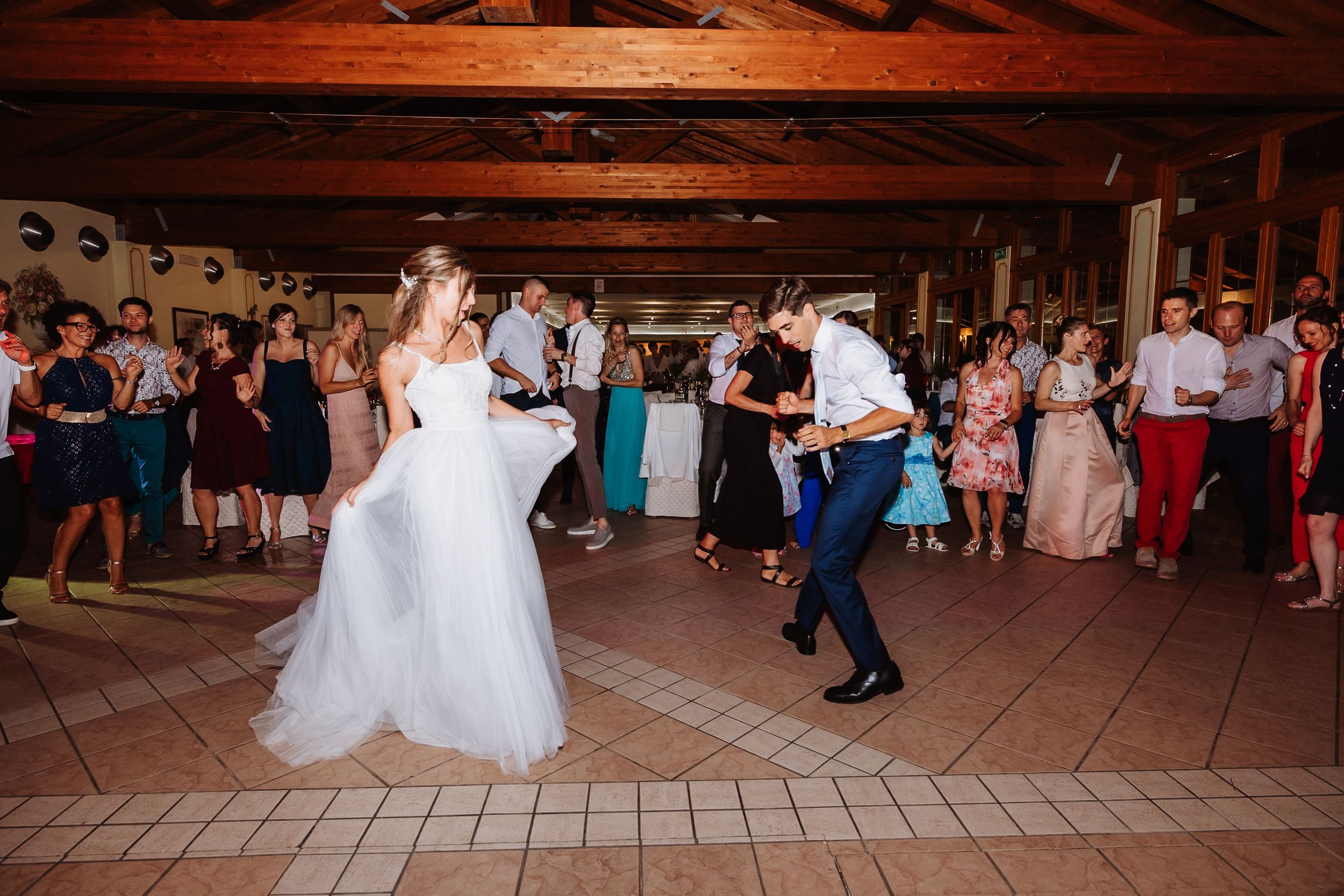 Wedding celebration with couples dancing on a wooden floor under rustic wooden beams.