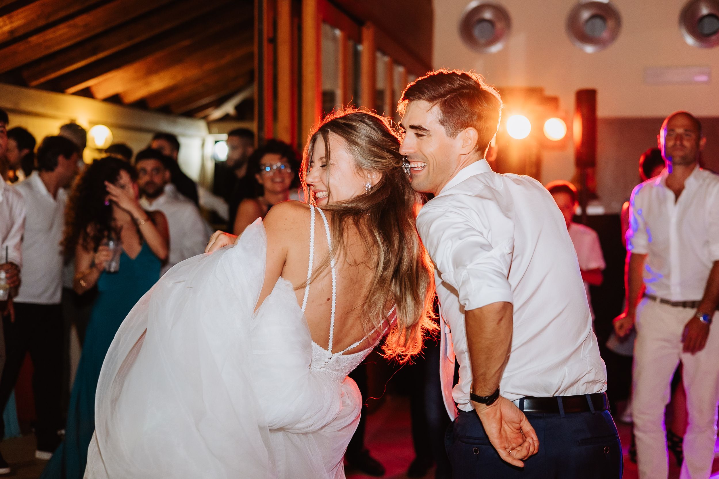 A couple dances together at a wedding reception venue with warm lighting and guests in the background.