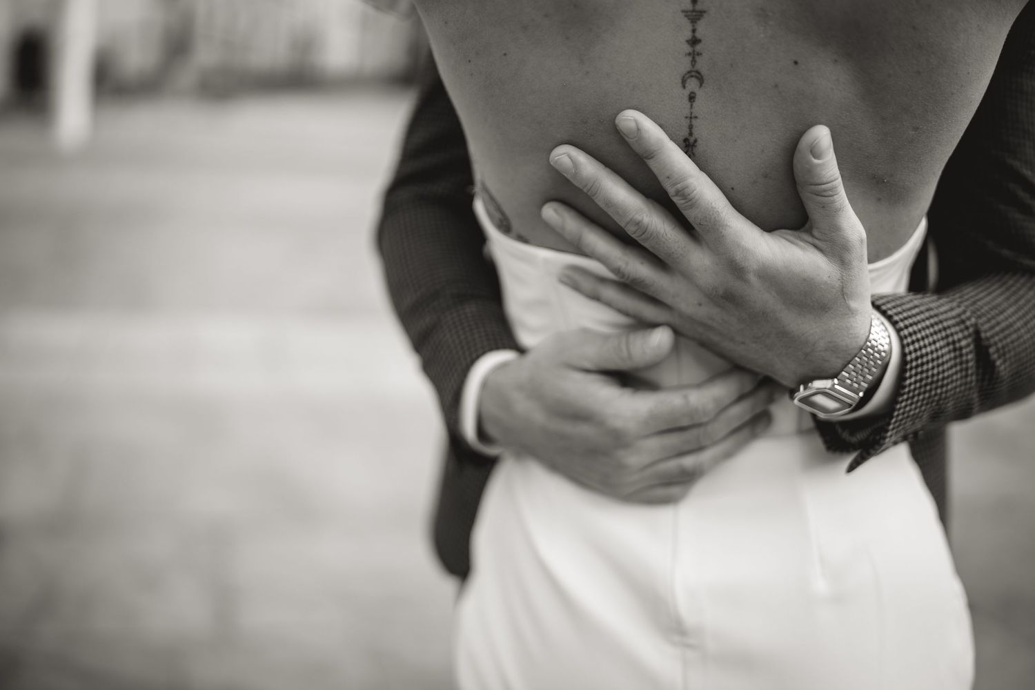 Close up black and white photo of a couple embracing, with hands clasped around each other, wearing formal attire.