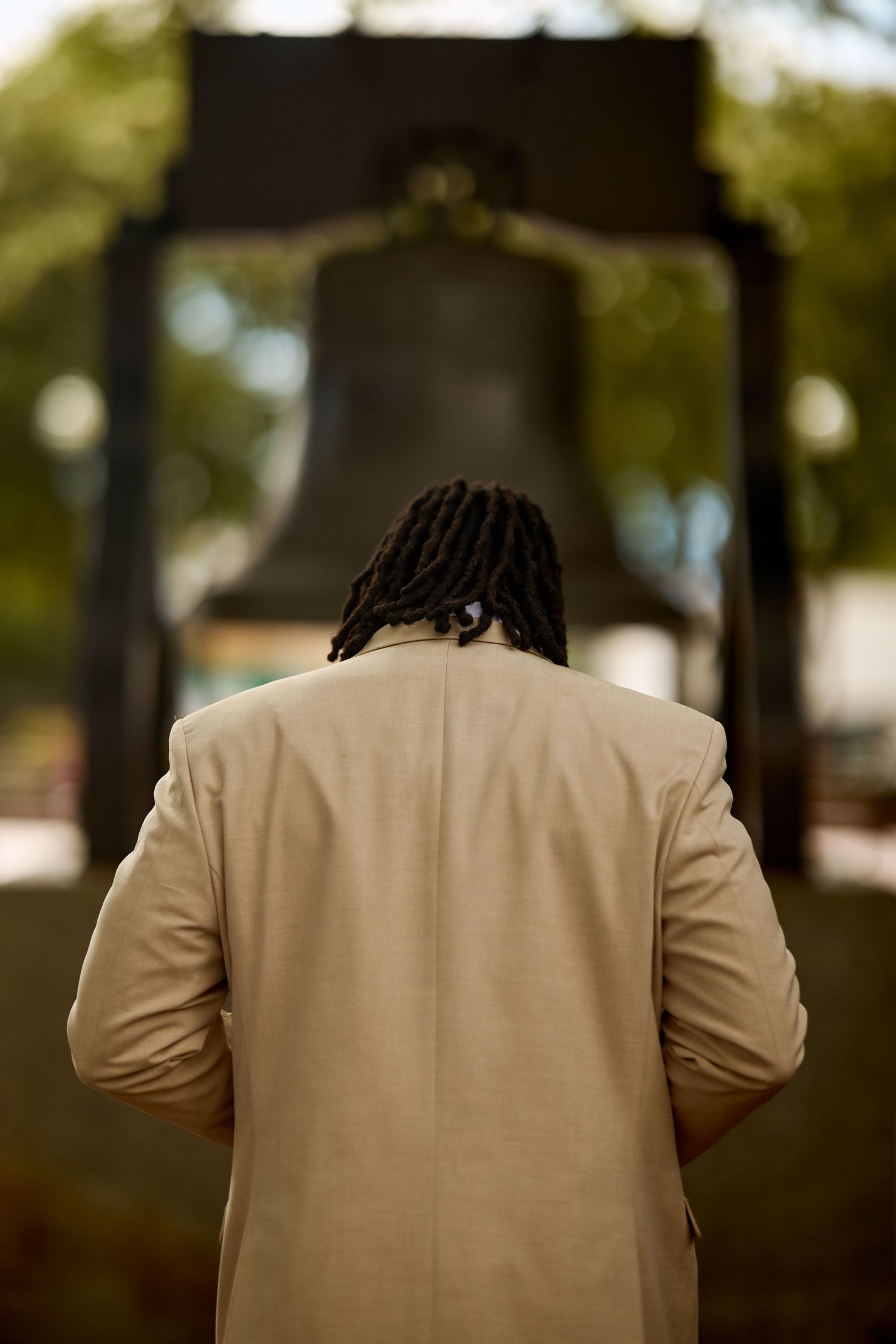 Back view of a person wearing a beige suit jacket sitting on a bench in an outdoor setting.