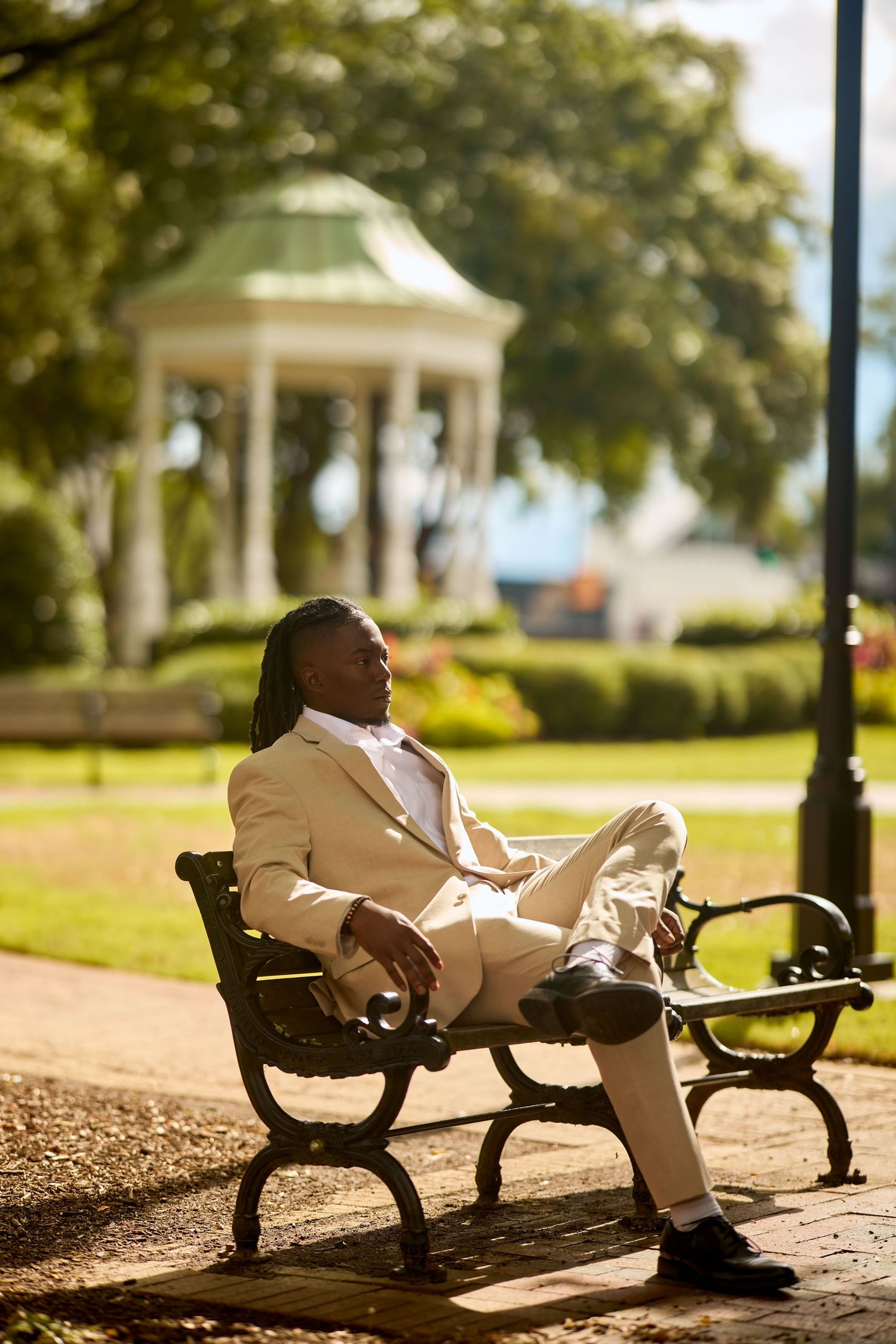Figure in white clothing lies comfortably on a row of decorative park benches on a sunny day.