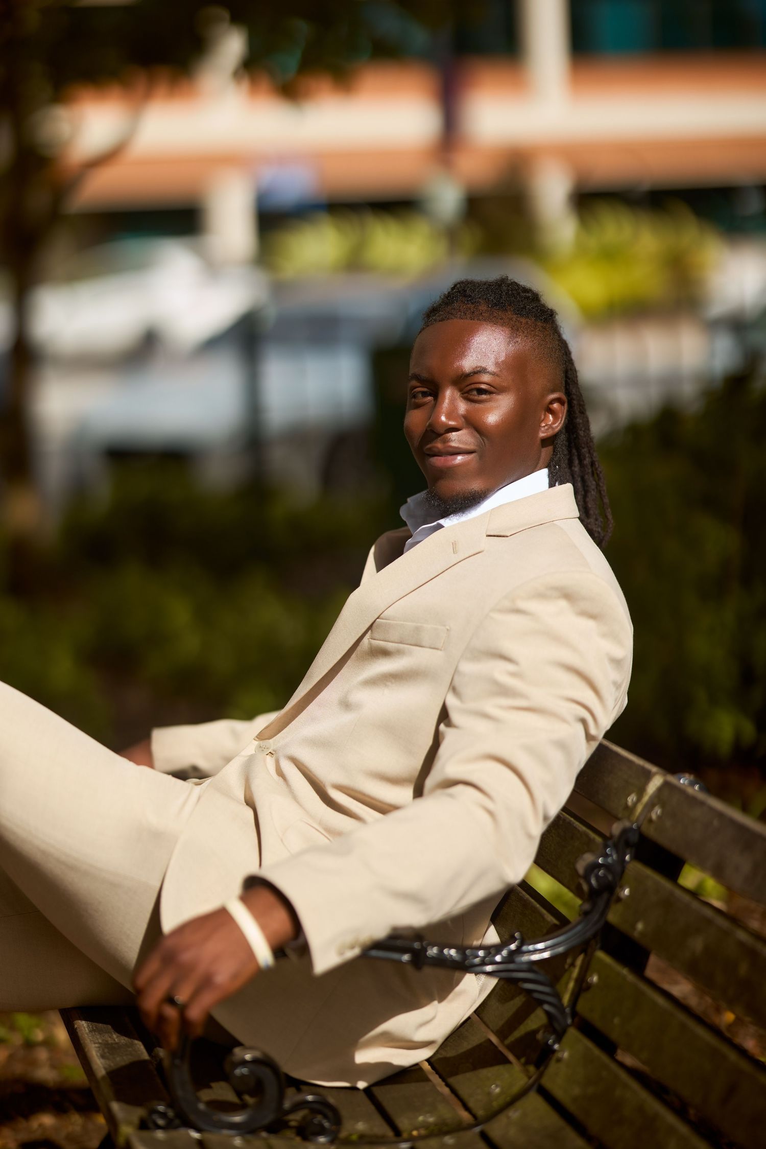 A person wearing a beige suit jacket reclines on a park bench with a content expression.