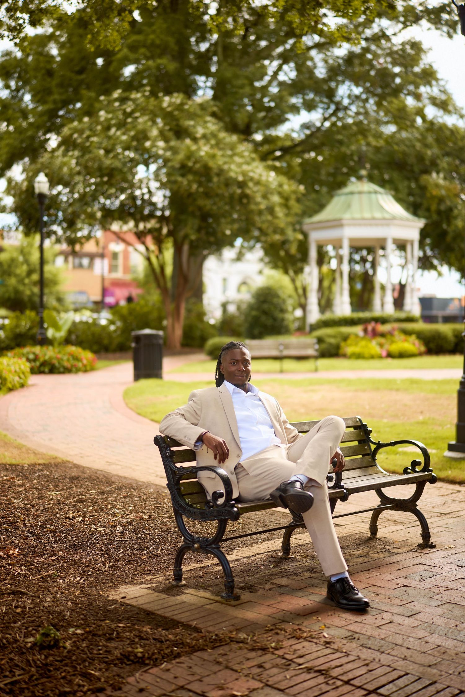 Someone relaxes on a park bench on a brick path surrounded by trees and landscaping at a scenic setting.