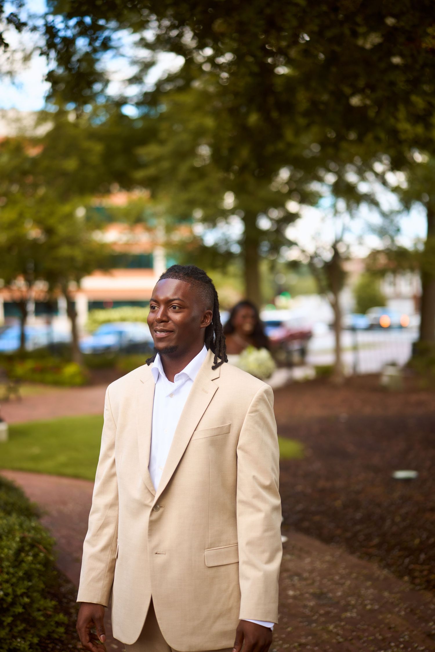 Professional portrait of someone wearing a light colored suit jacket against a blurred outdoor background.