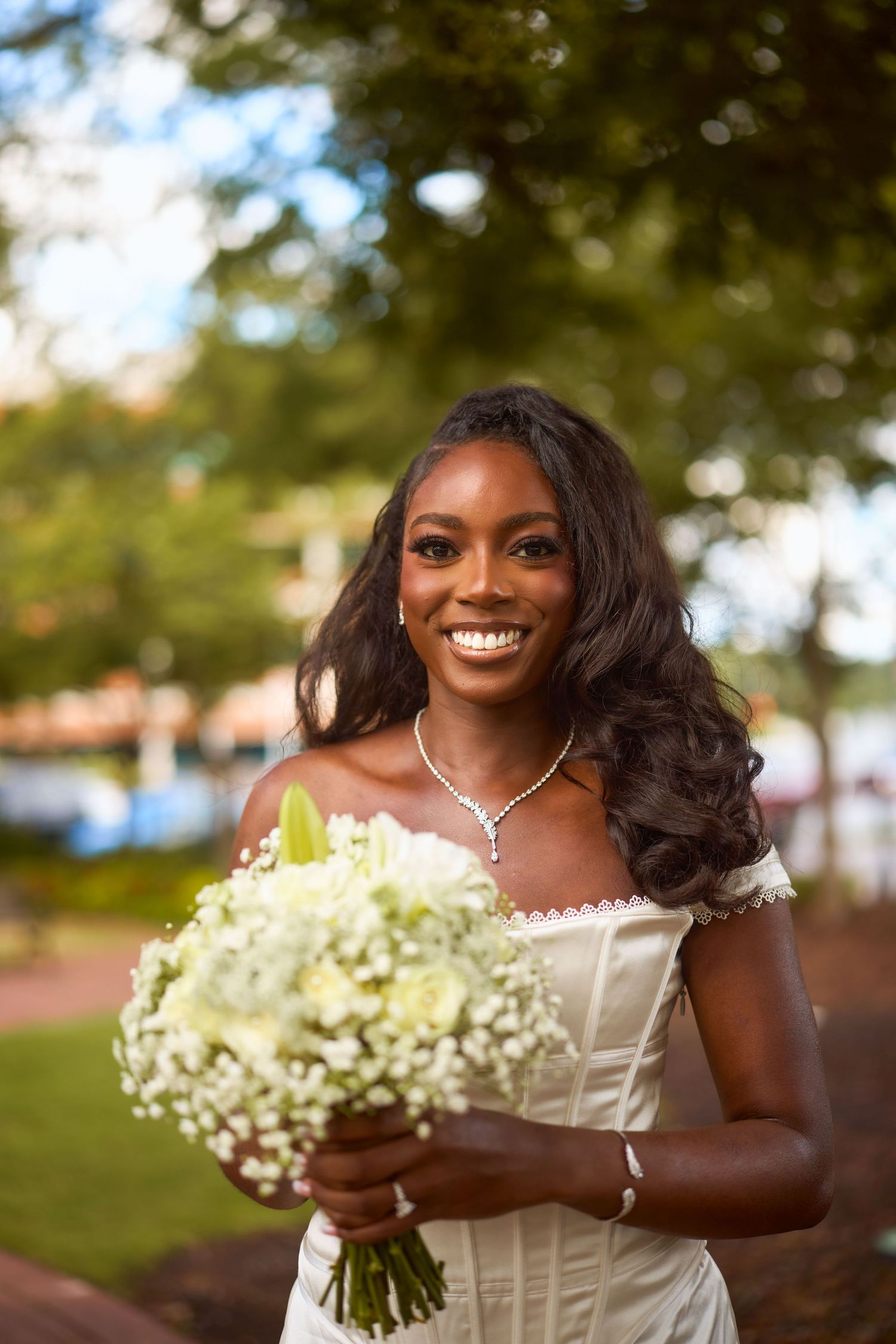 A radiant bride holds a beautiful bouquet of baby's breath flowers while posing outdoors during golden hour.