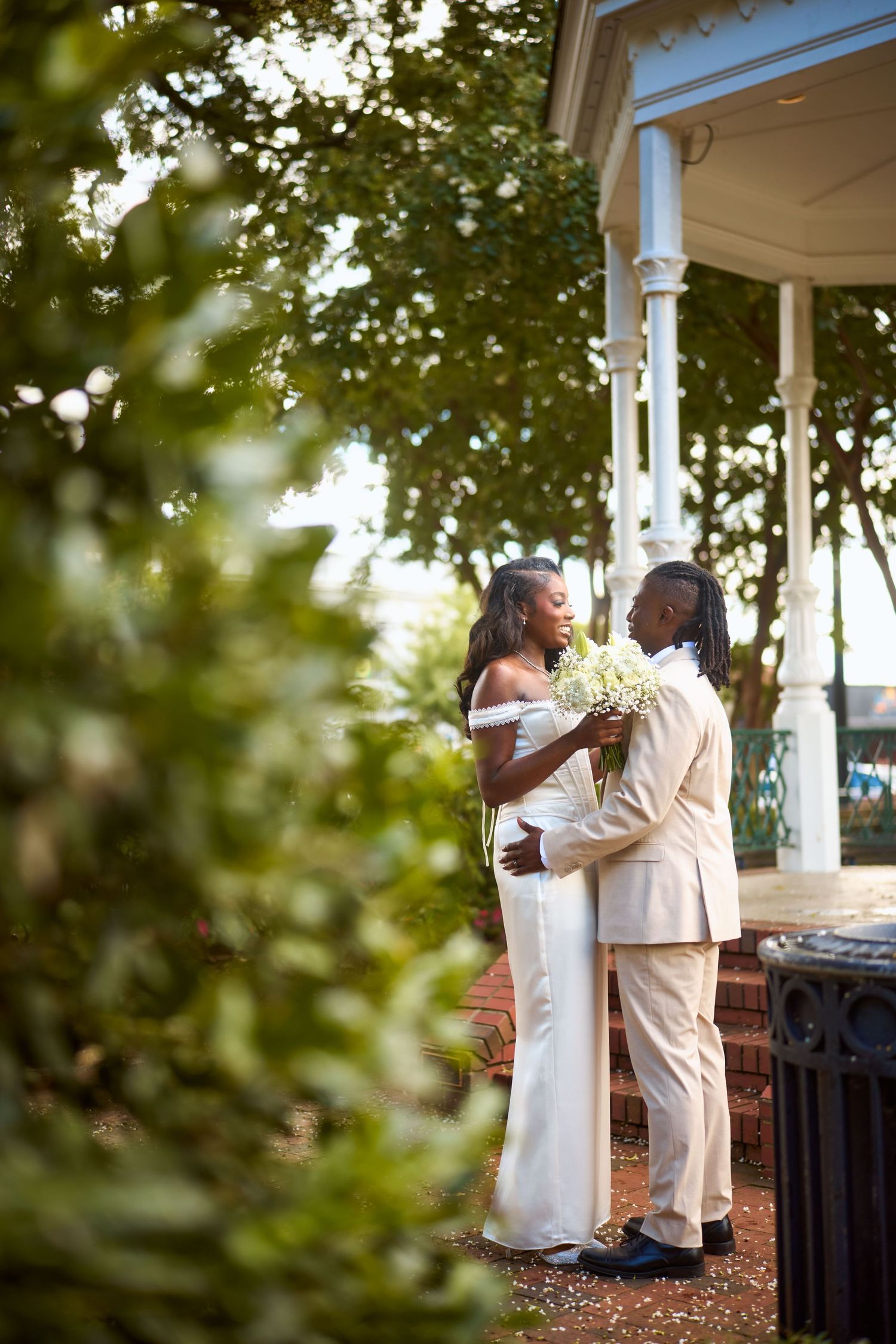 A romantic couple shares tender moments outdoors in an elegant gazebo during a wedding celebration.