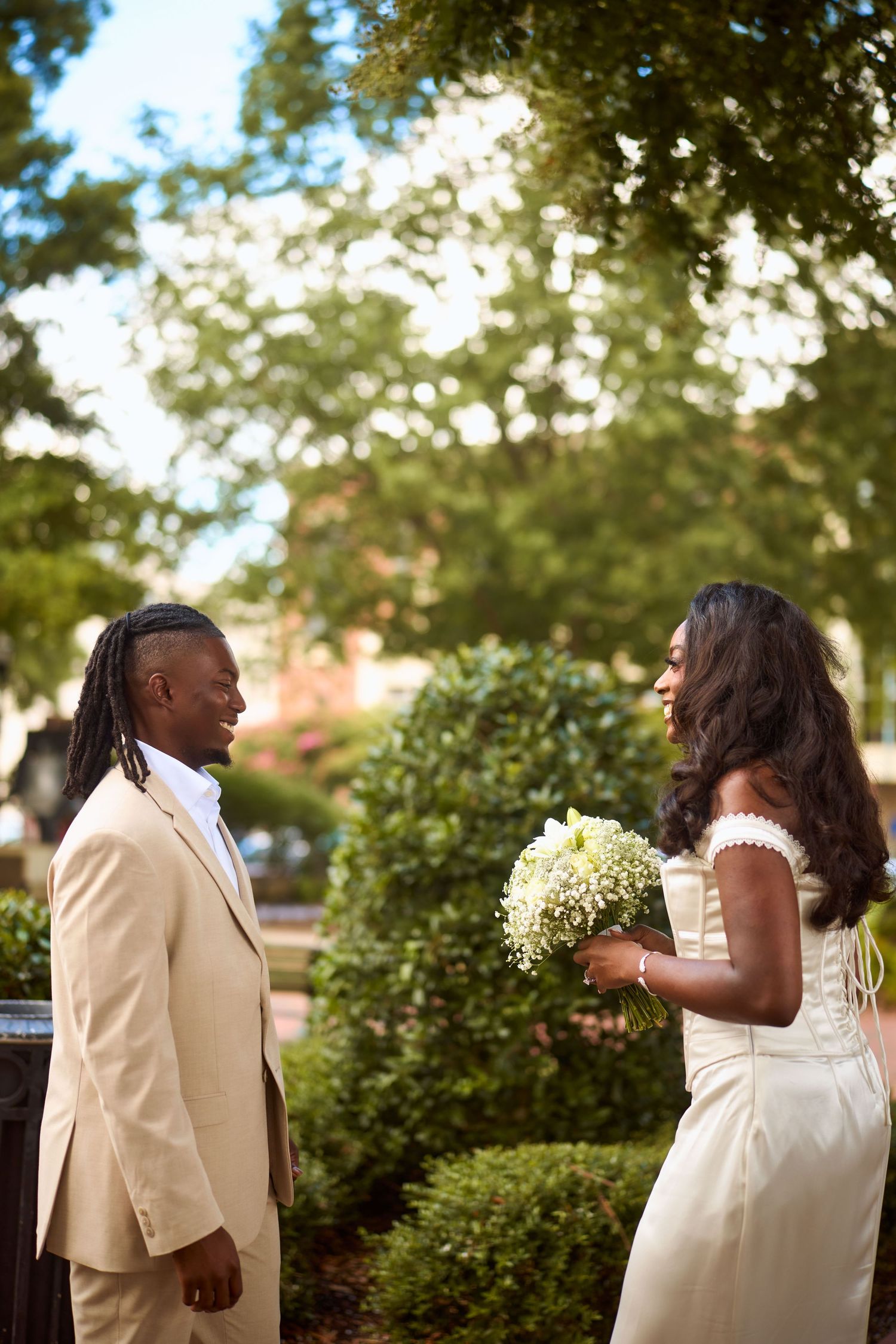 A couple shares tender moments in a garden setting while wearing elegant white outfits.