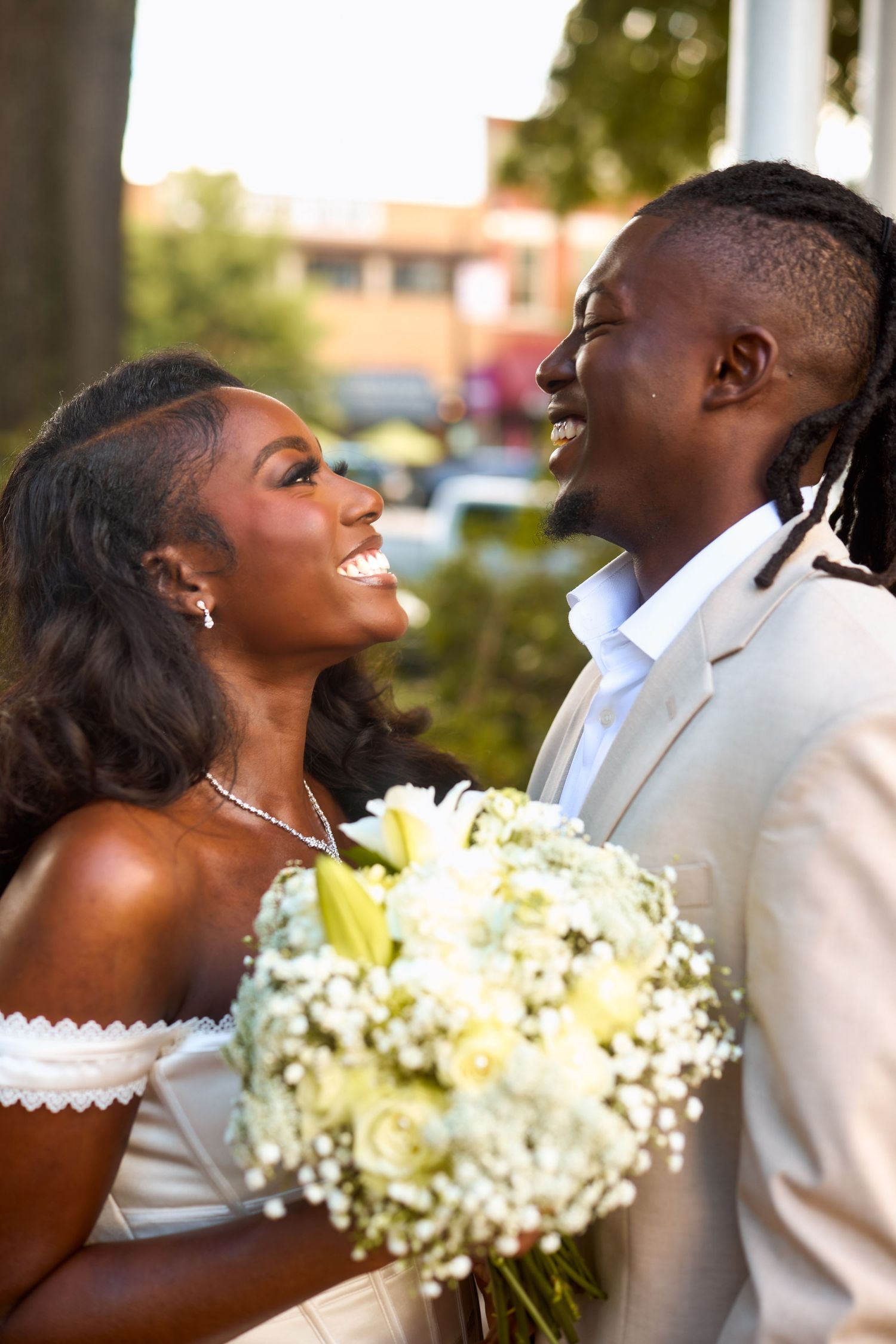 Joyful couple shares a candid moment on their wedding day with the bride holding a beautiful bouquet of white flowers.