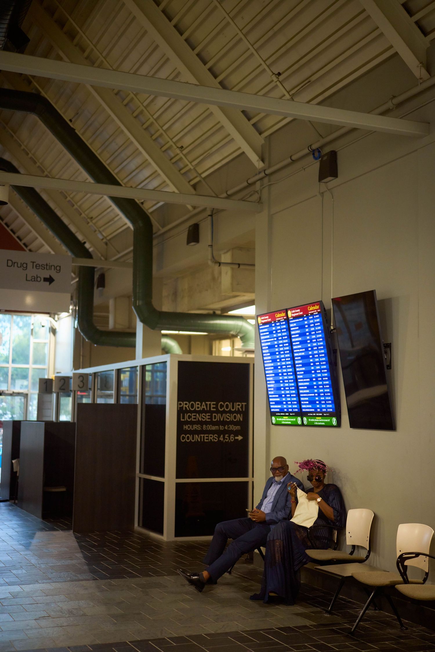 Dimly lit terminal lounge area with blue digital flight information displays and waiting area seating.
