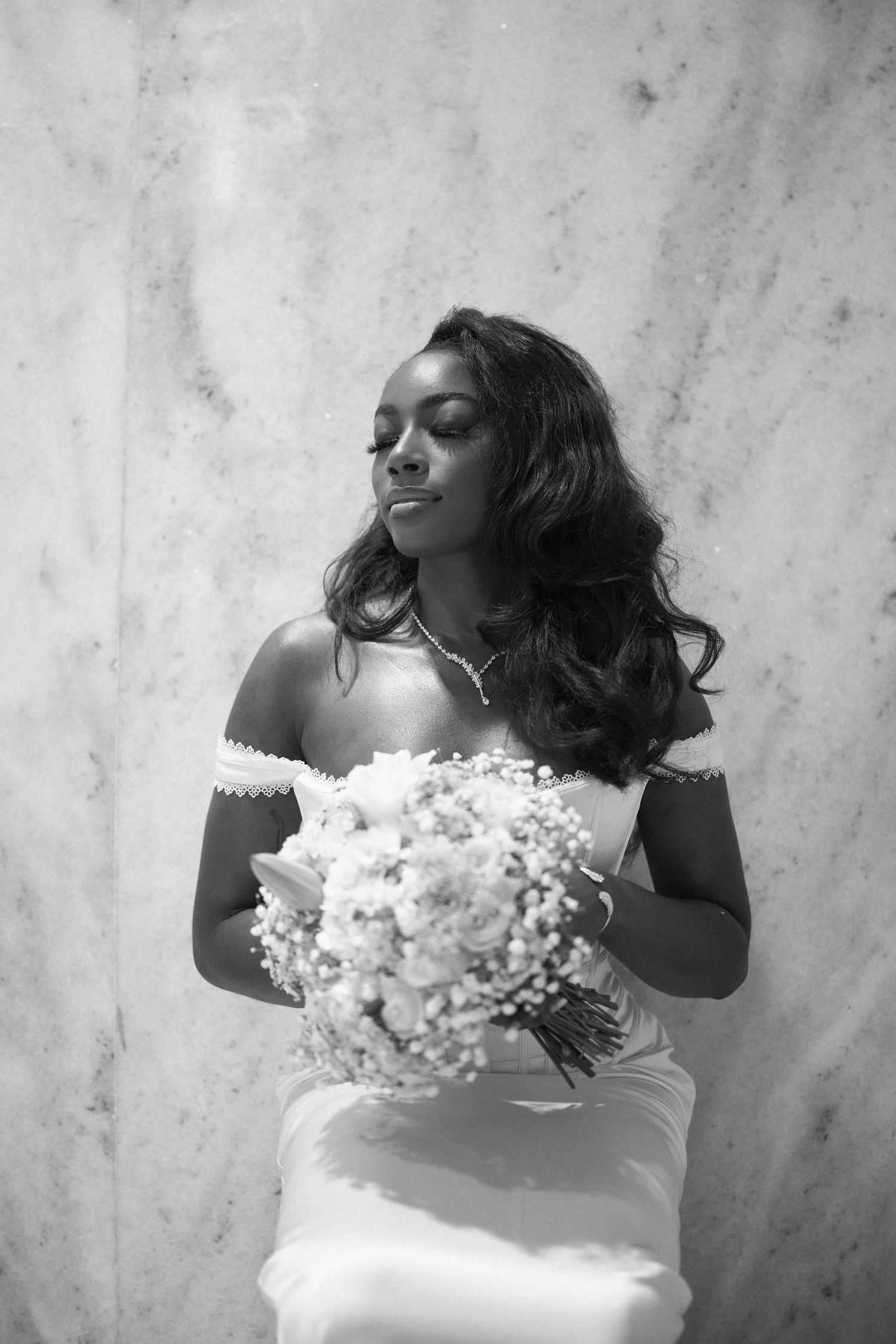 Black and white artistic sequence of a person in a white dress holding white flowers against a textured wall.