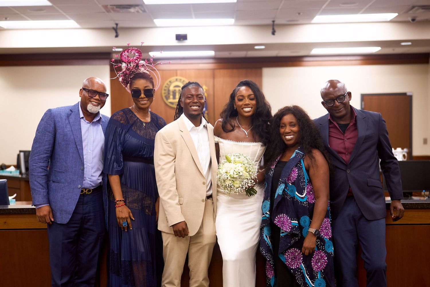 A group of six people dressed formally pose together at what appears to be an indoor event or gathering.