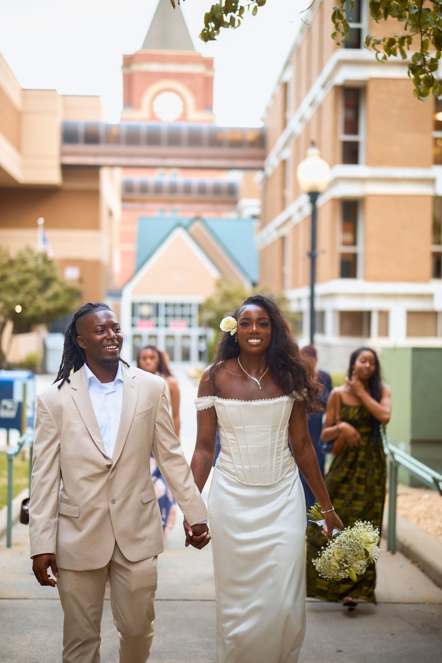 A happy couple dressed in wedding attire share joyful laughter while walking outdoors near a building.