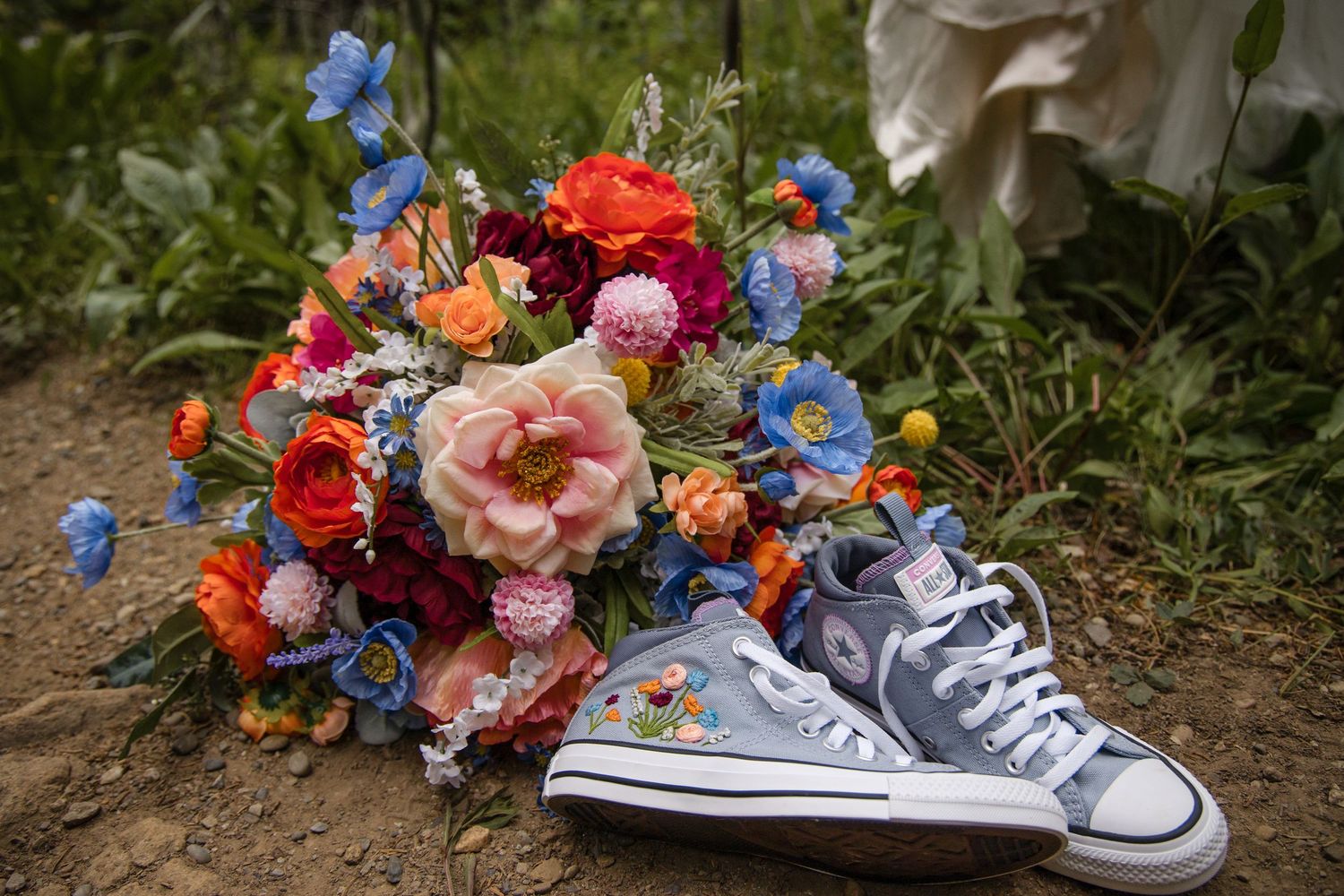 Colorful floral arrangements with blue and orange blooms laid beside classic sneakers in an outdoor garden setting.