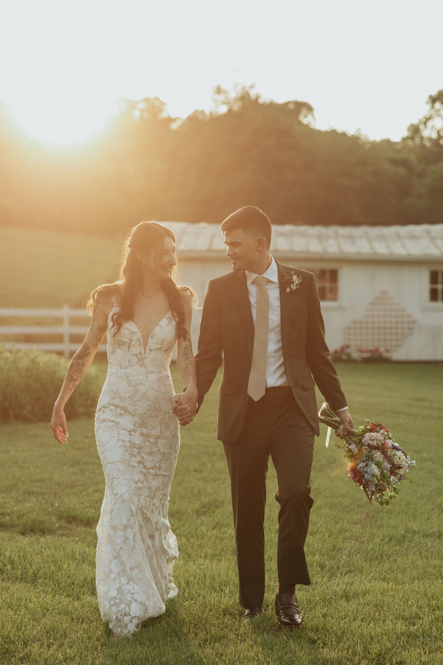 A couple walking hand in hand through a grassy field at golden hour in their wedding attire.