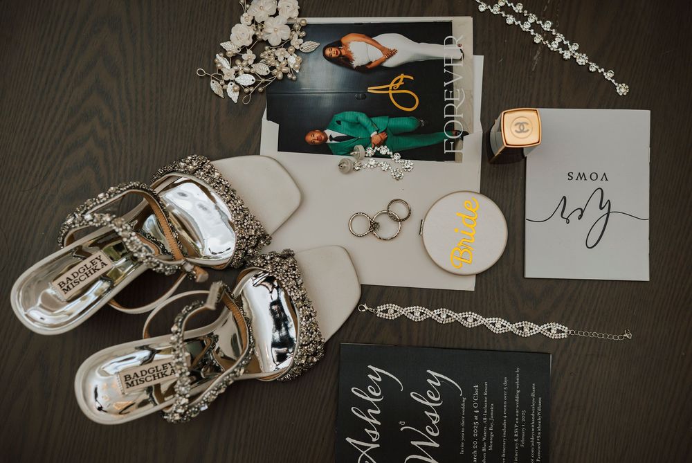 Wedding details flatlay with rings, jewelry, and invitation cards arranged on dark background.