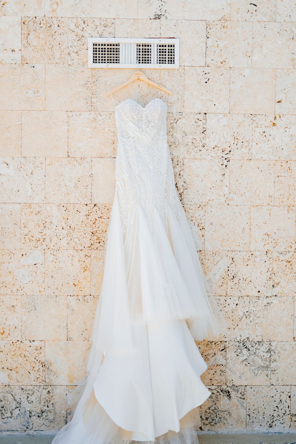 A white wedding dress hangs against a textured stone wall in a progression of five similar photos.