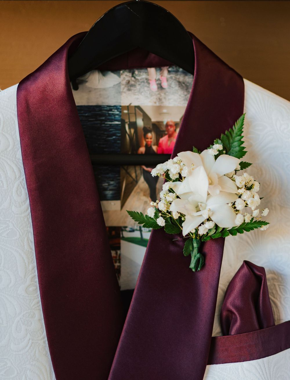 Close-up of burgundy colored suit jackets with white floral boutonnieres pinned to the lapels.