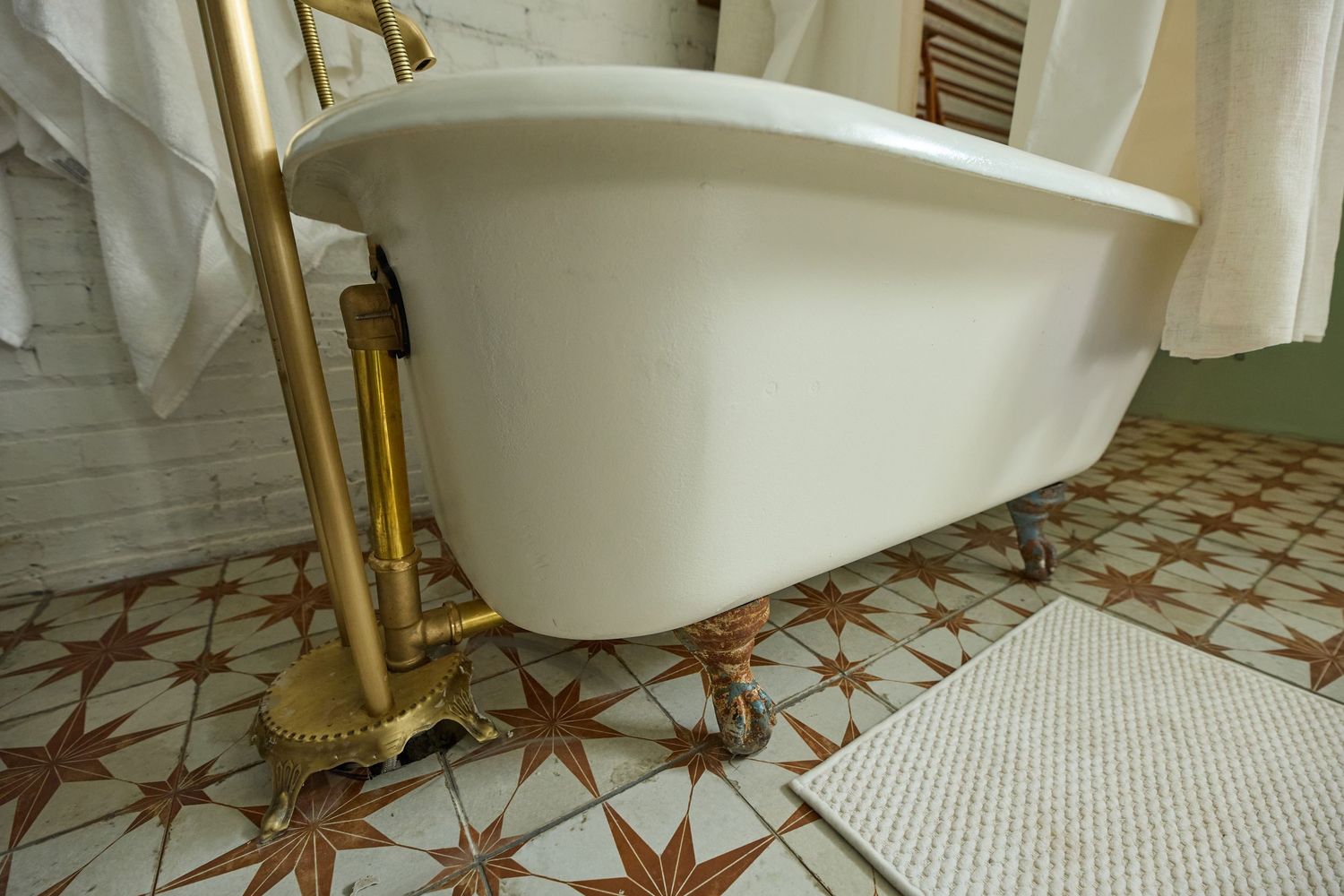White clawfoot bathtub with gold fixtures on patterned tile flooring.